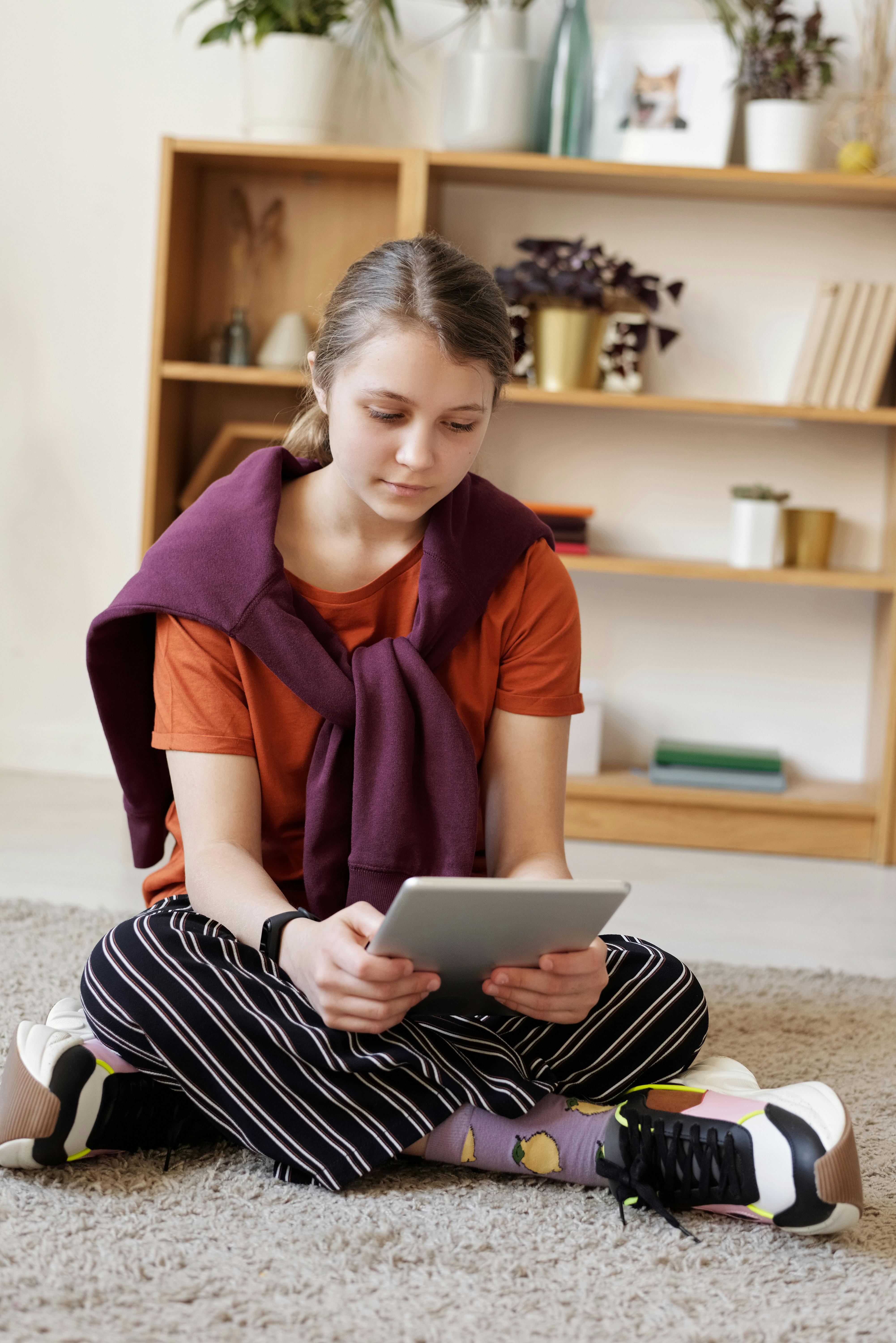A teenage girl sitting on the floor using a tablet | Source: Pexels