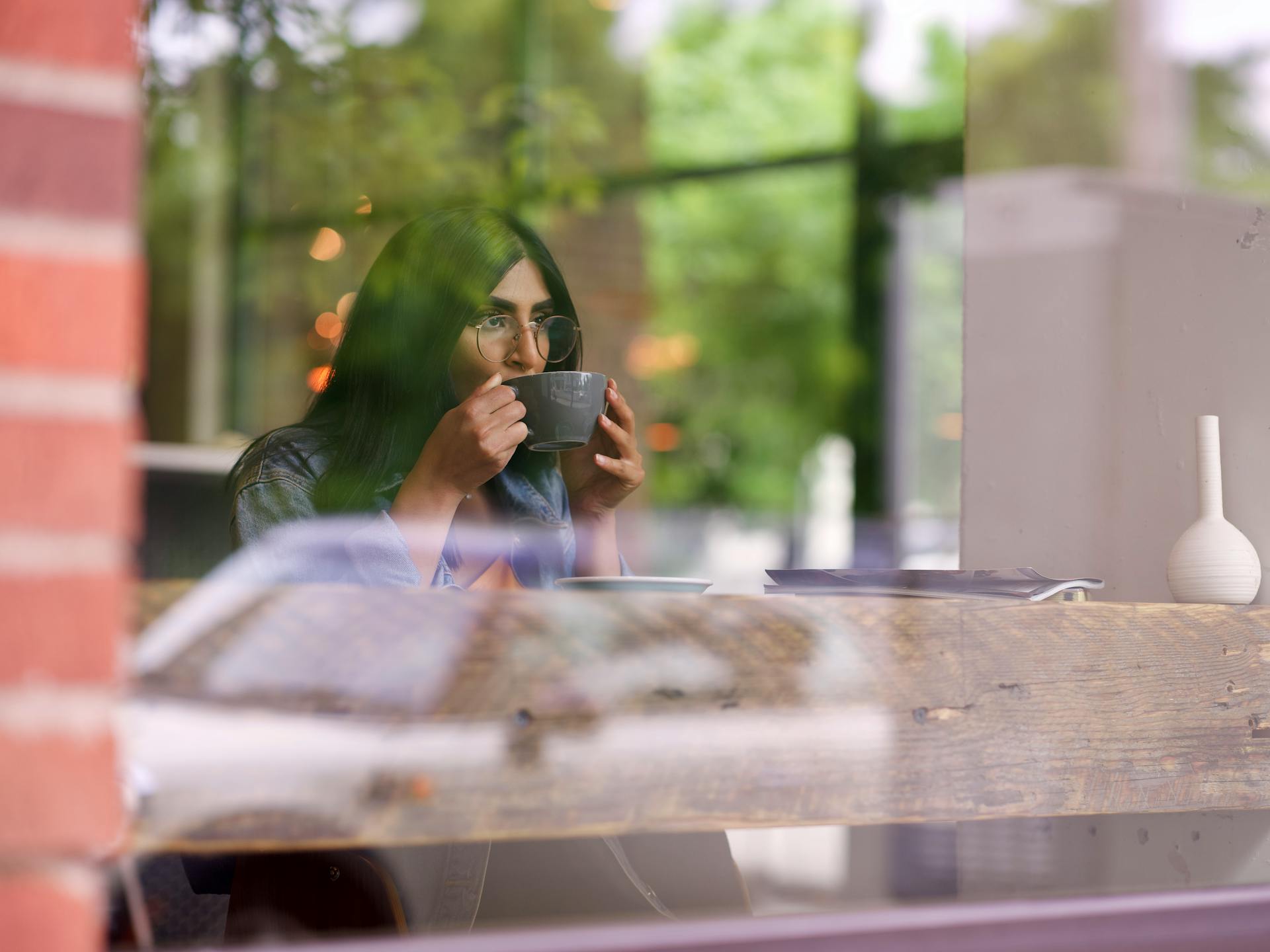 A woman sitting in a café and drinking from a mug while looking outside from the window | Source: Pexels
