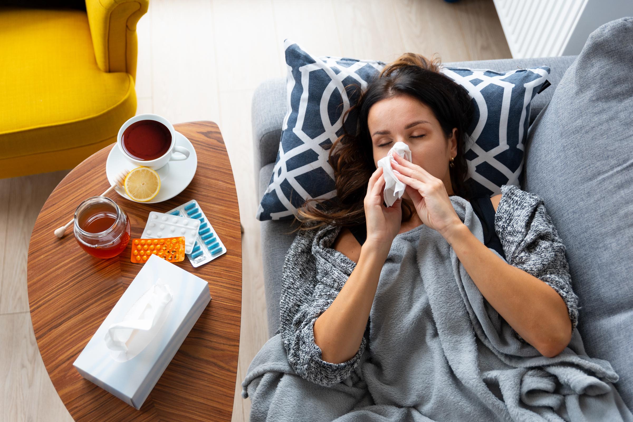 A sick woman rests on the couch, managing cold or flu symptoms with medication and common remedies for upper respiratory infections | Source: Getty Images