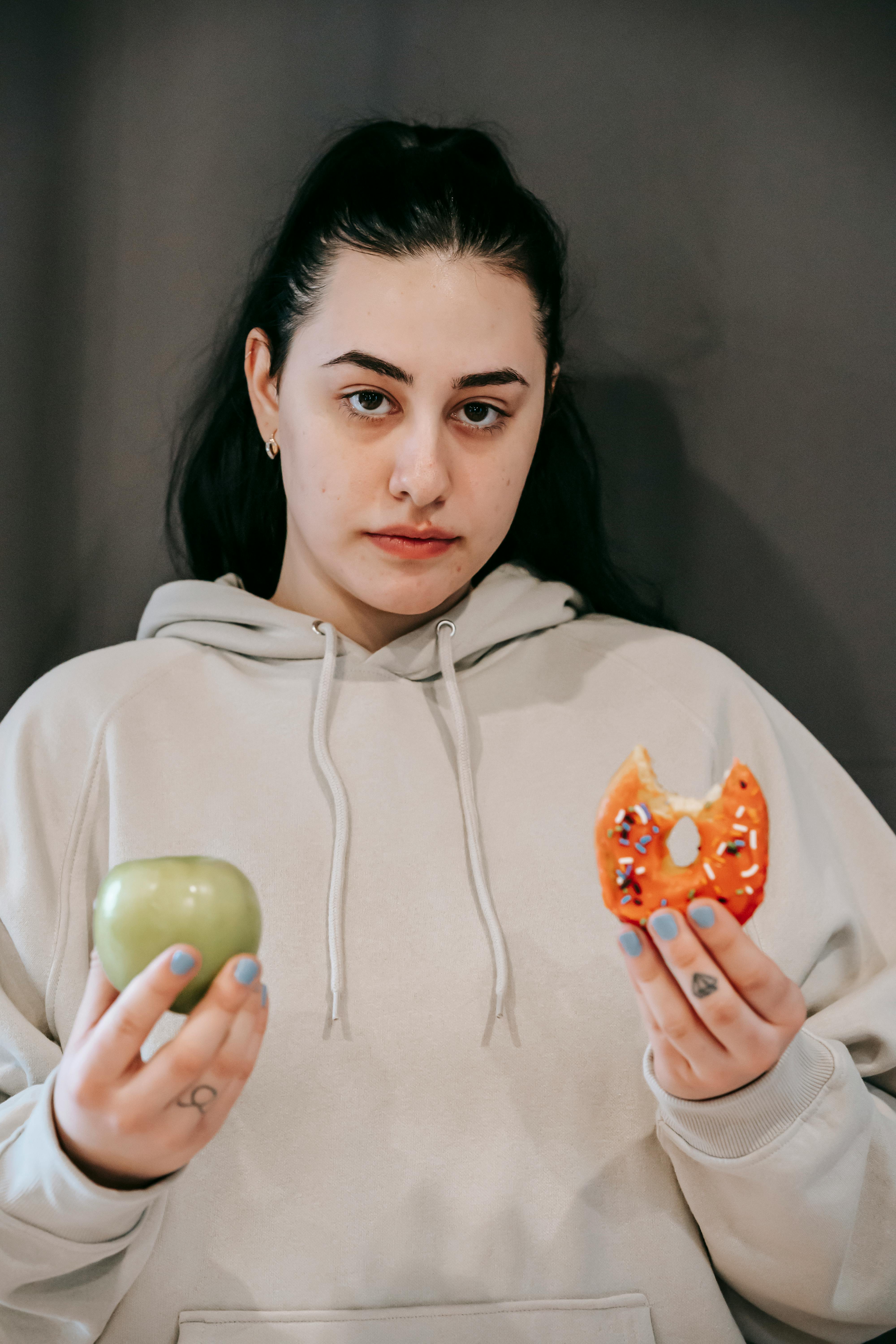 A woman holding an apple and a donut | Source: Pexels