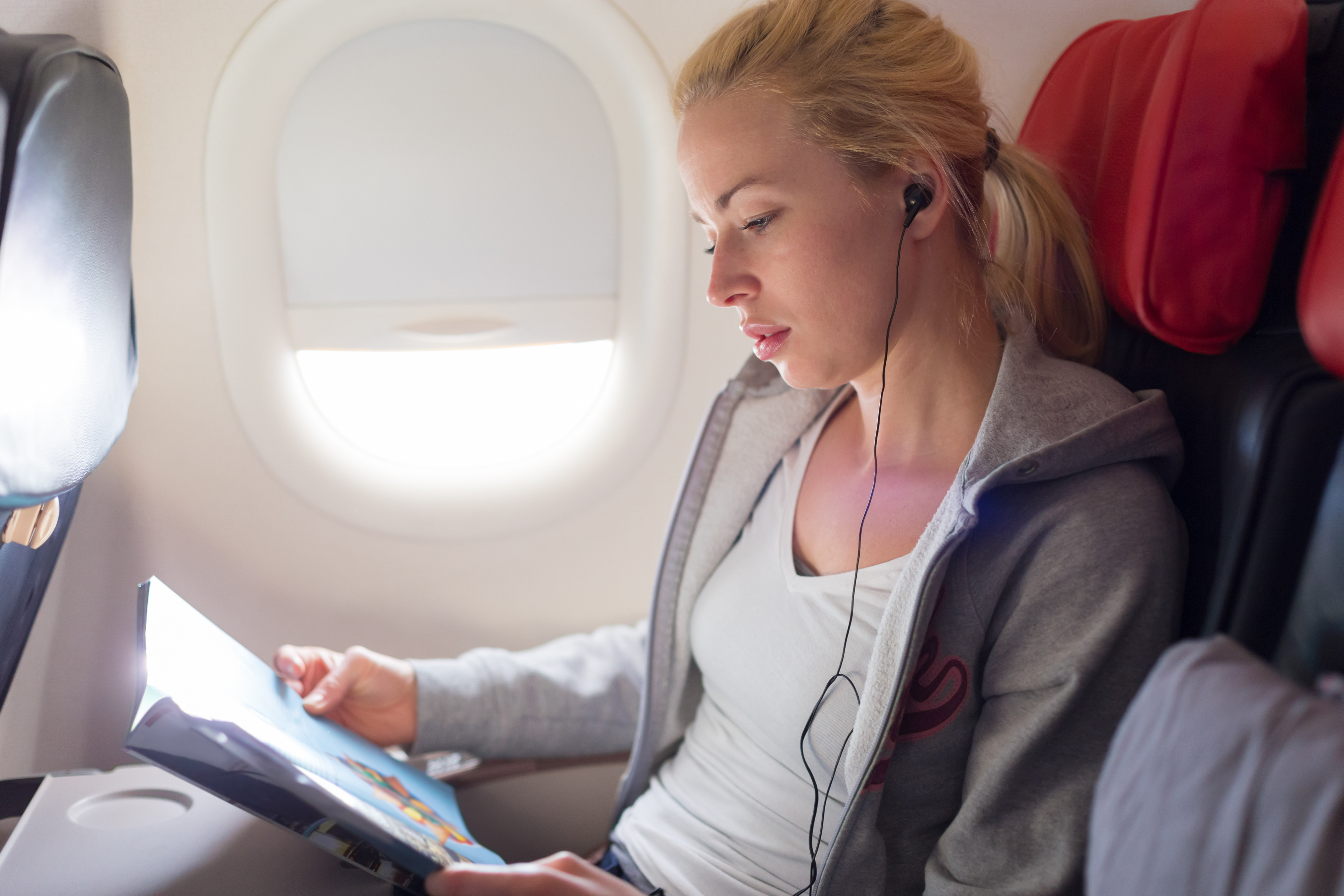 A woman reads a magazine and listens to music on an airplane. | Source: Shutterstock