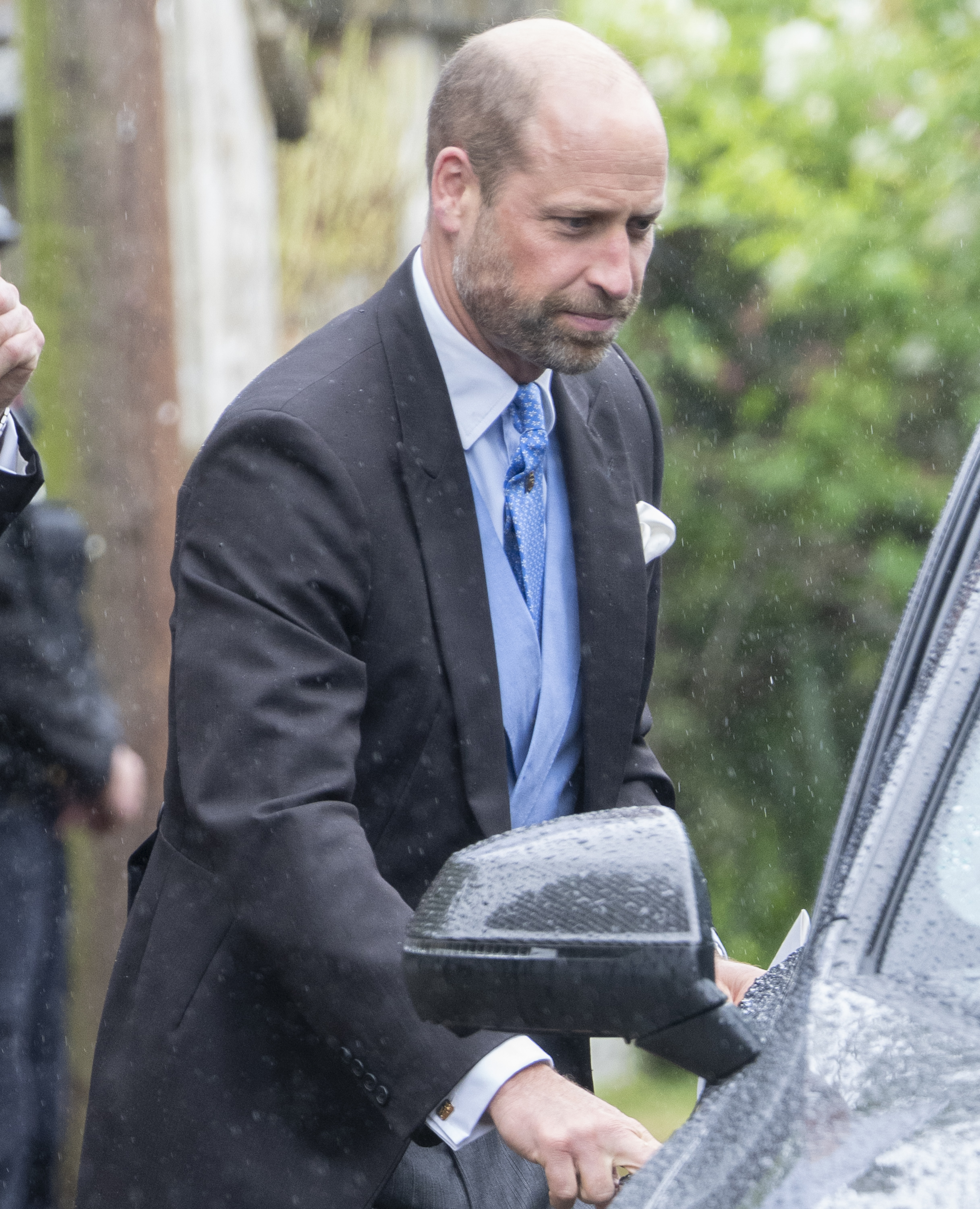 Prince William arrives at the wedding venue in the rain, wearing a classic morning suit accented with a light blue waistcoat and patterned tie. | Source: Getty Images