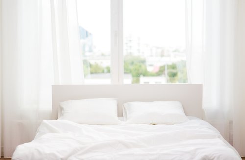 A bed with white linen under a window. | Photo: Shutterstock