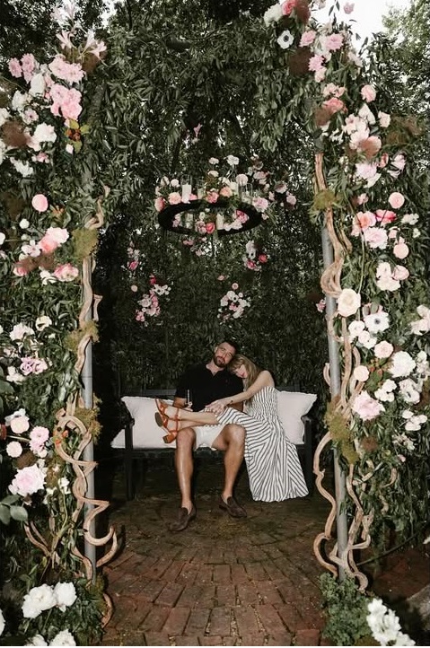 Taylor Swift and Travis Kelce sitting on a bench under a flower arch after getting engaged, from her post dated August 26, 2025 | Source: Instagram/taylorswift