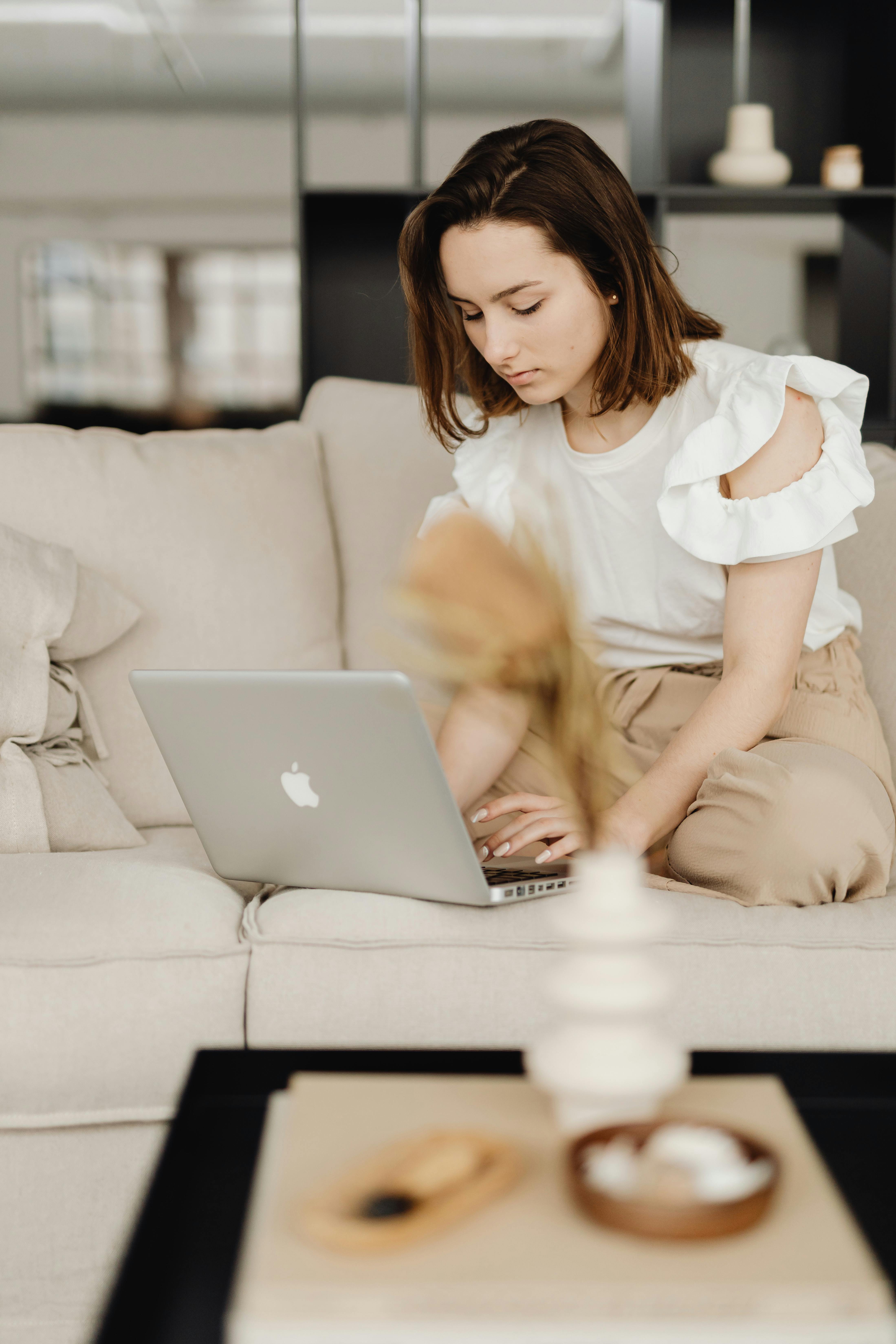 A woman on the couch typing on a Macbook | Source: Pexels