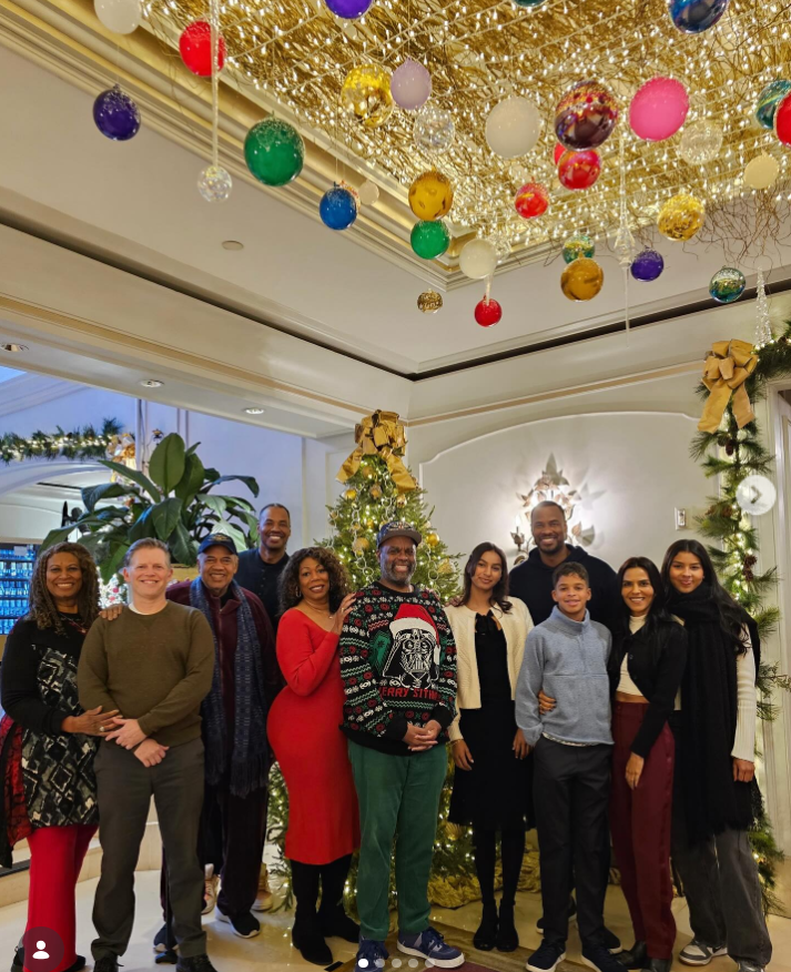 Jason Collins poses with family and friends in a festively decorated hotel lobby surrounded by glowing Christmas trees, hanging ornaments, and holiday lights during a group celebration. | Source: Instagram/jasoncollins_98