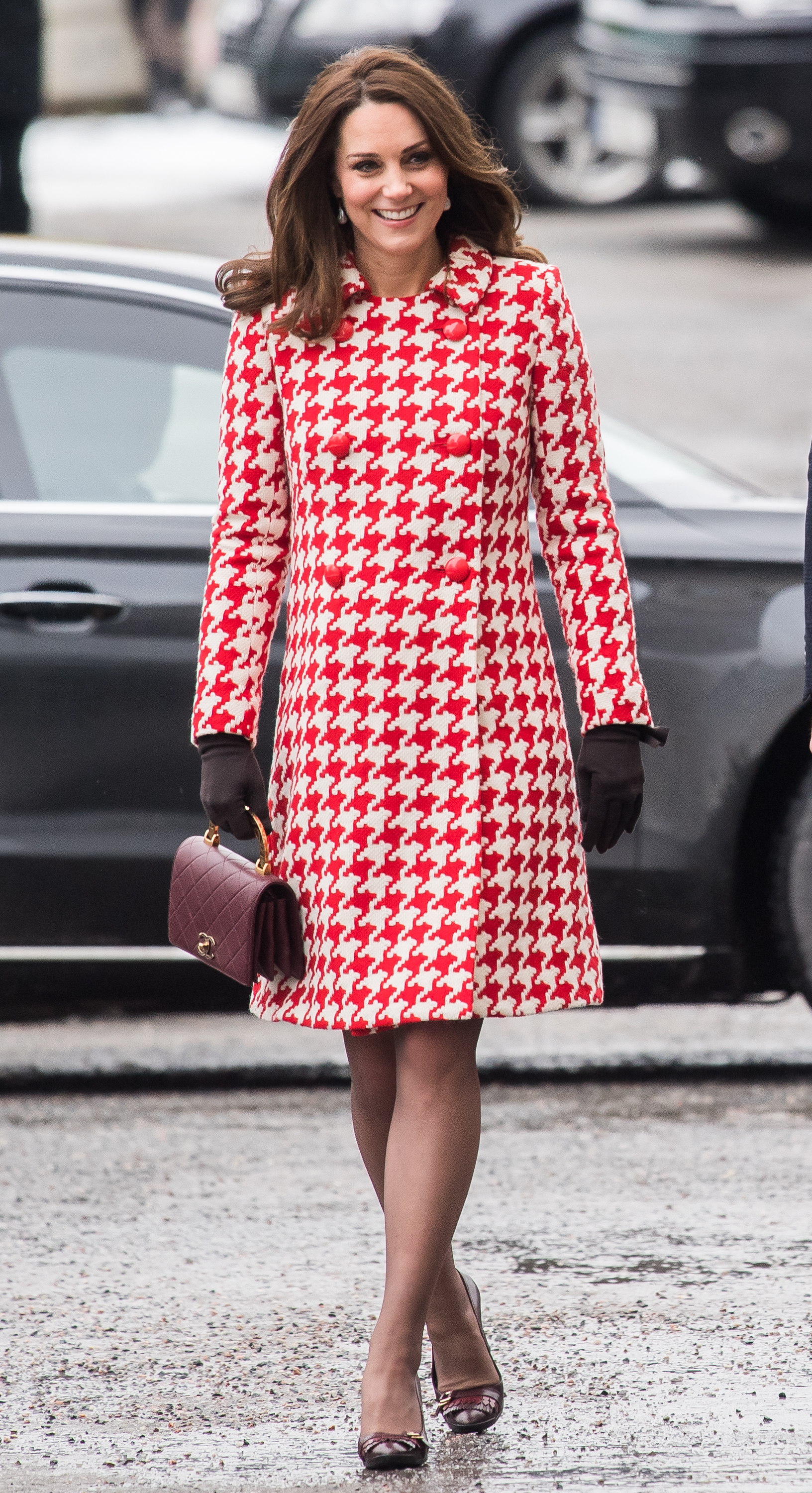 During a royal visit to Sweden on January 31, 2018, Princess Catherine arrives at the Karolinska Institute in a bold red-and-white houndstooth coat. Her rich, chestnut hair is softly curled and worn down, complementing the tailored winter look.