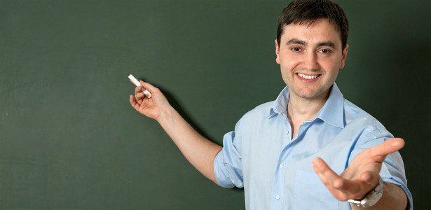 A male teacher holding a chalk in front of a blackboard. | Photo: Flickr