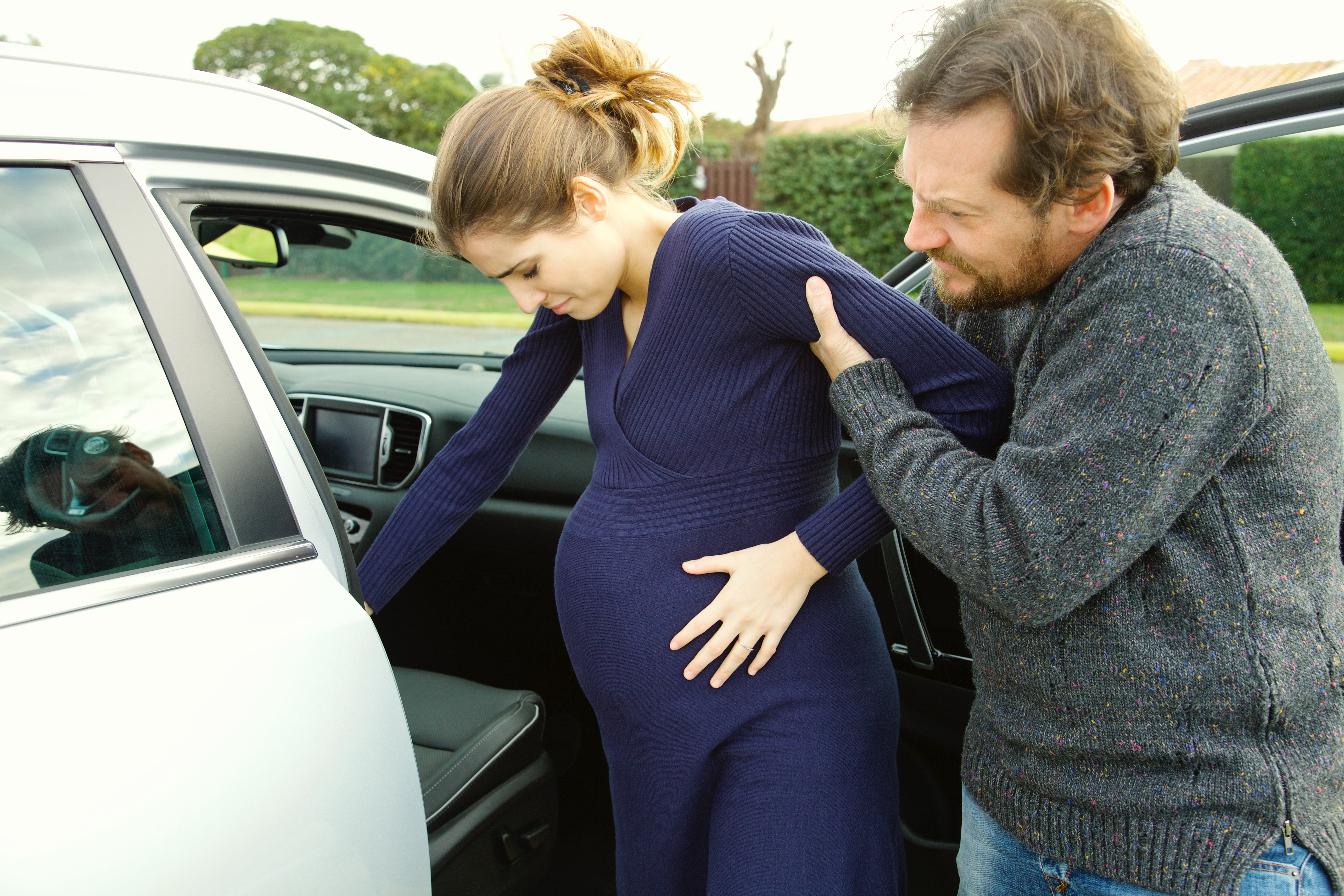 A heavily pregnant woman getting help from a man to enter a car | Source: Shutterstock