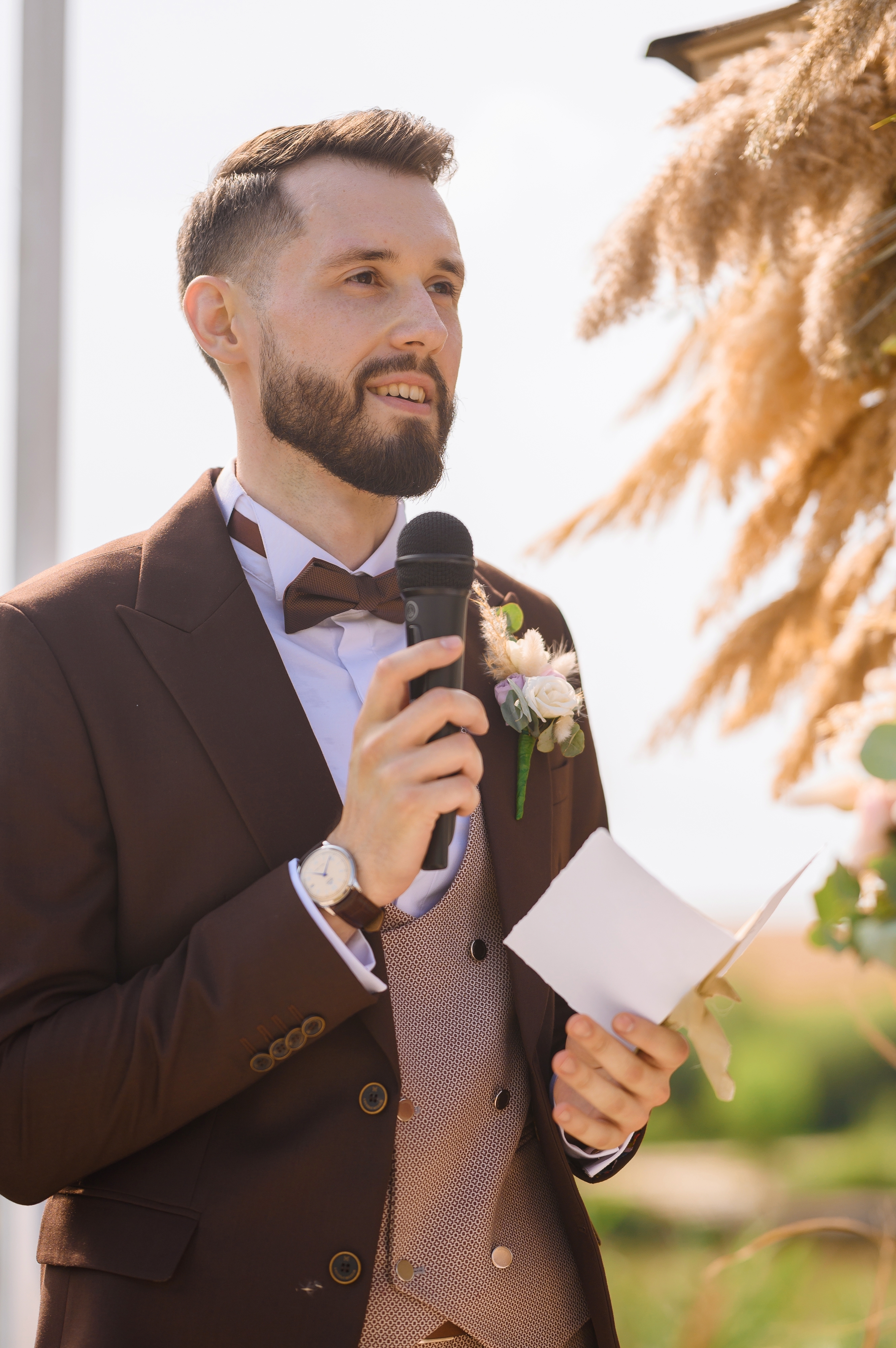 A man dressed in a brown suit with a boutonniere and bow tie giving a speech at a wedding | Source: Shutterstock