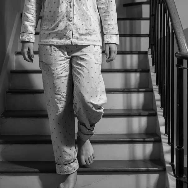 A figure in pyjamas walking down a flight of stairs | Source: Midjourney