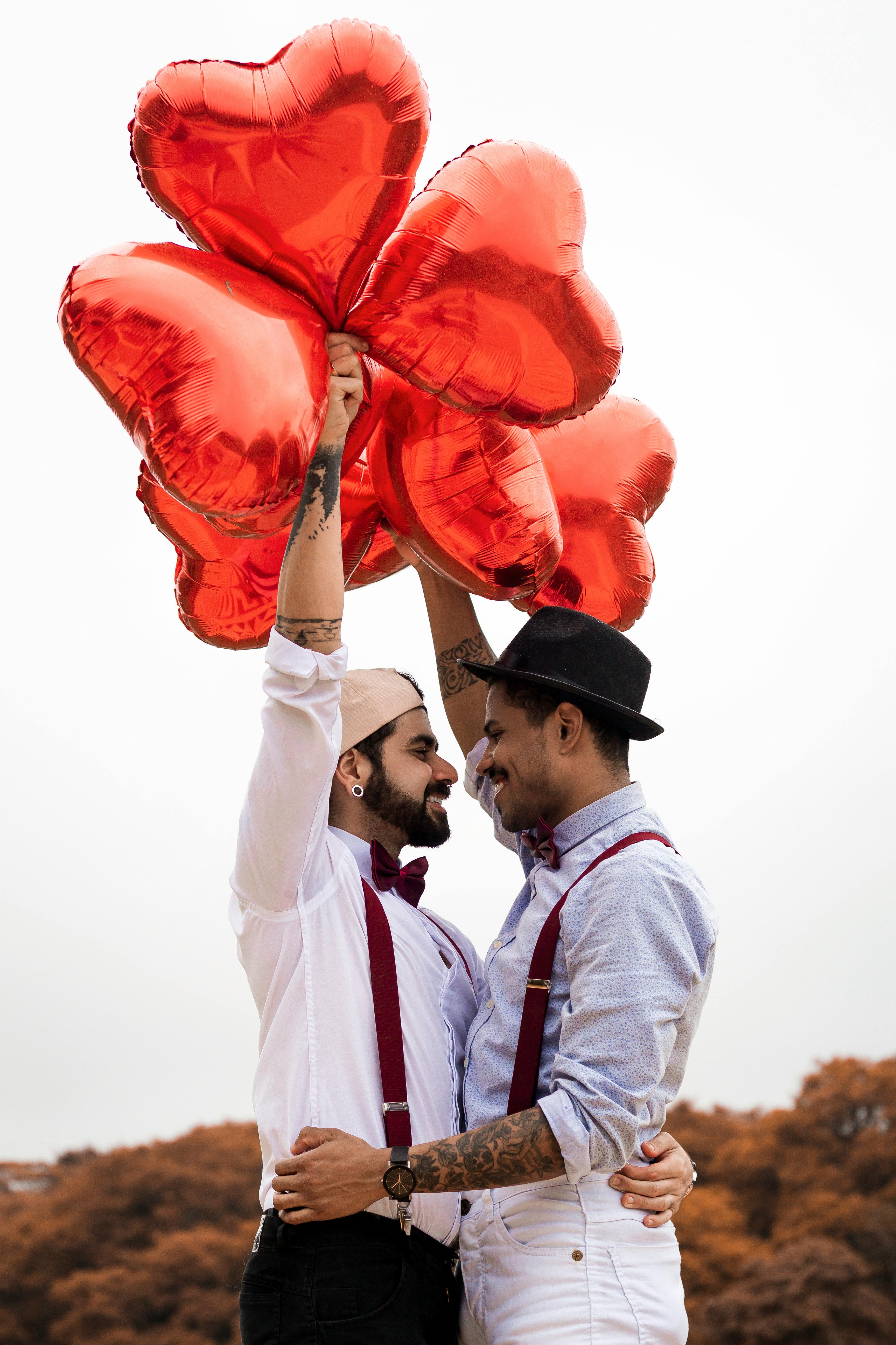 Two men embracing while holding heart balloons | Source: Pexels