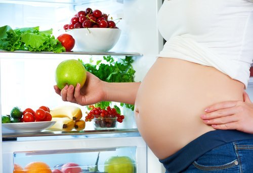 Mujer embarazada que se coloca cerca del refrigerador con las frutas y verduras. | Foto: Shutterstock Mujer embarazada que se coloca cerca del refrigerador con las frutas y verduras. | Foto: Shutterstock