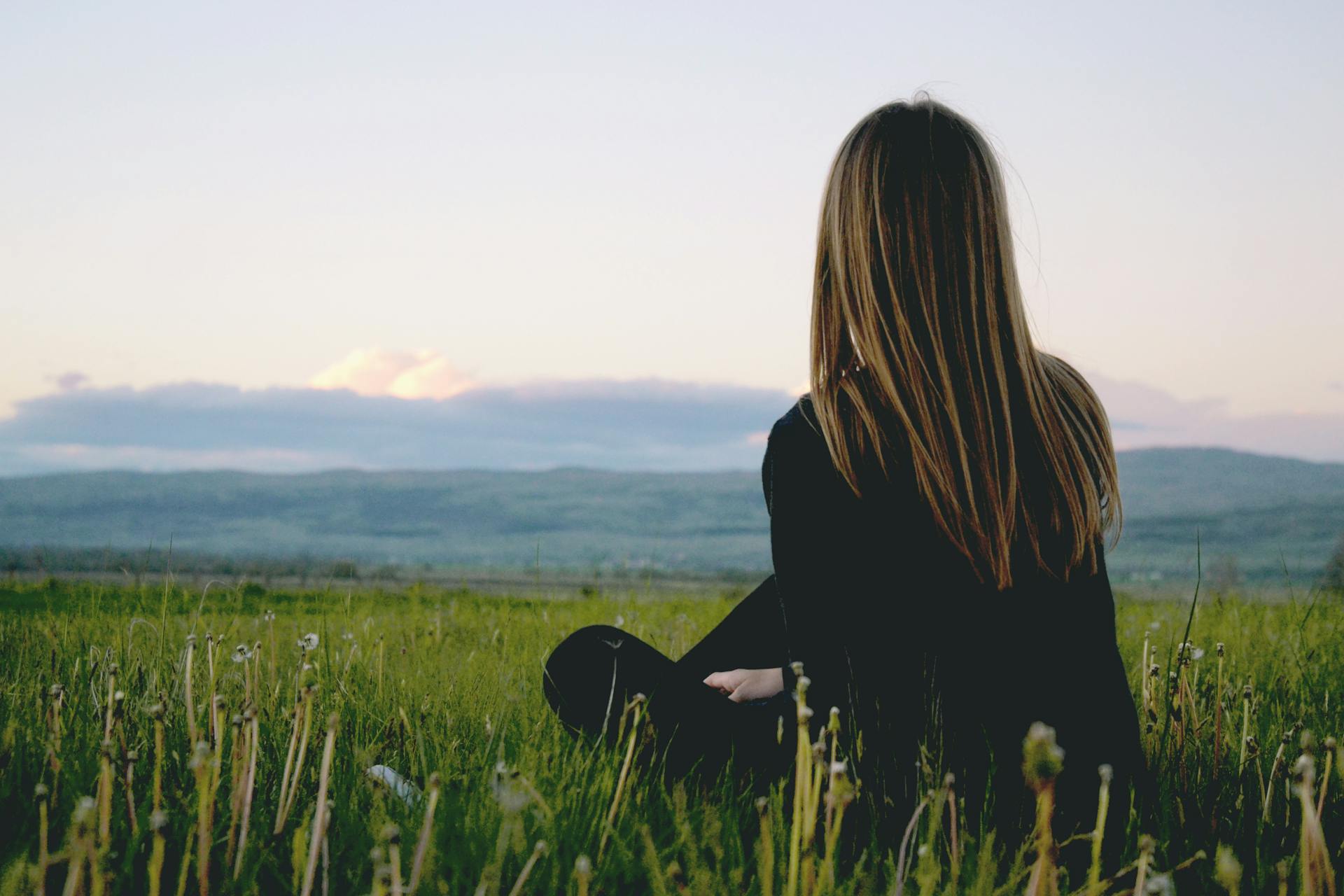 A back view of a woman sitting in a green field | Source: Pexels