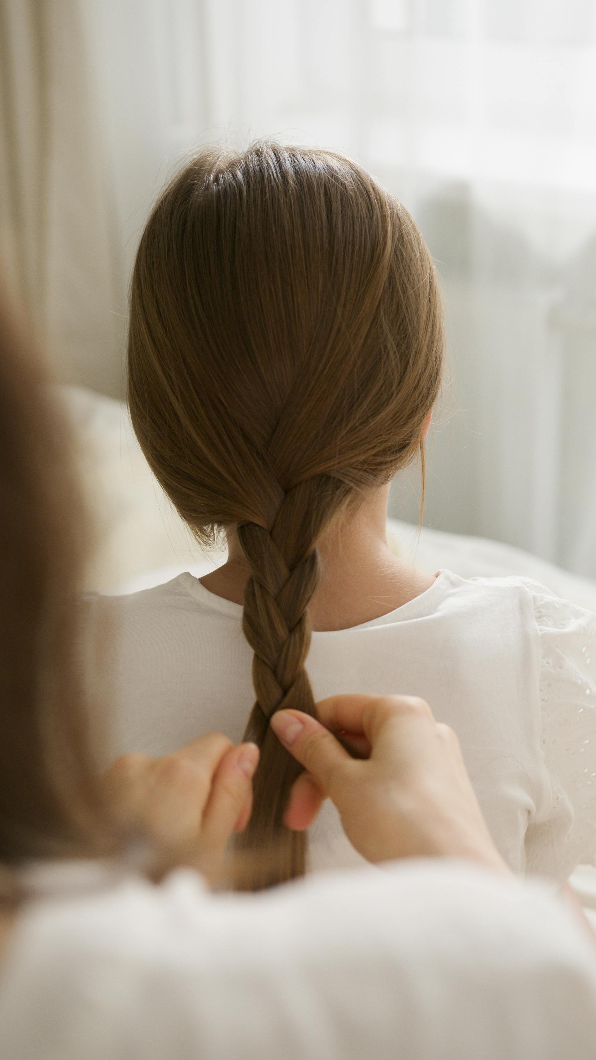 Close-up shot of a woman braiding her daughter's hair | Source: Pexels