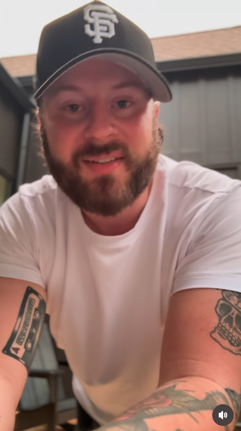 Nate Smith leans toward the camera in a fitted white T-shirt and black San Francisco Giants cap, giving followers a closer look at his noticeably slimmer appearance. | Source: Instagram/natesmith