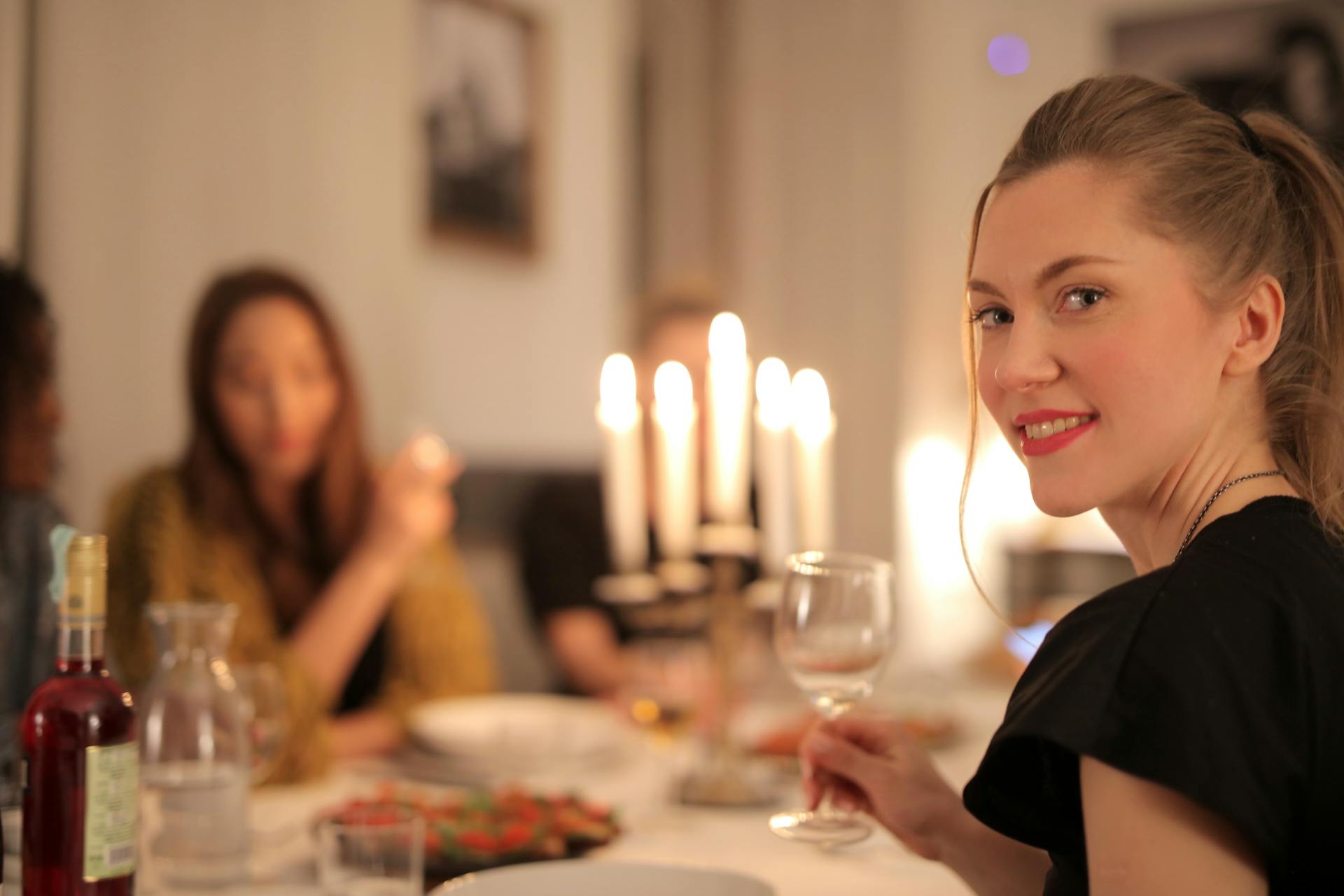 A woman smiles while holding a glass of wine at the dinner table | Source: Pexels