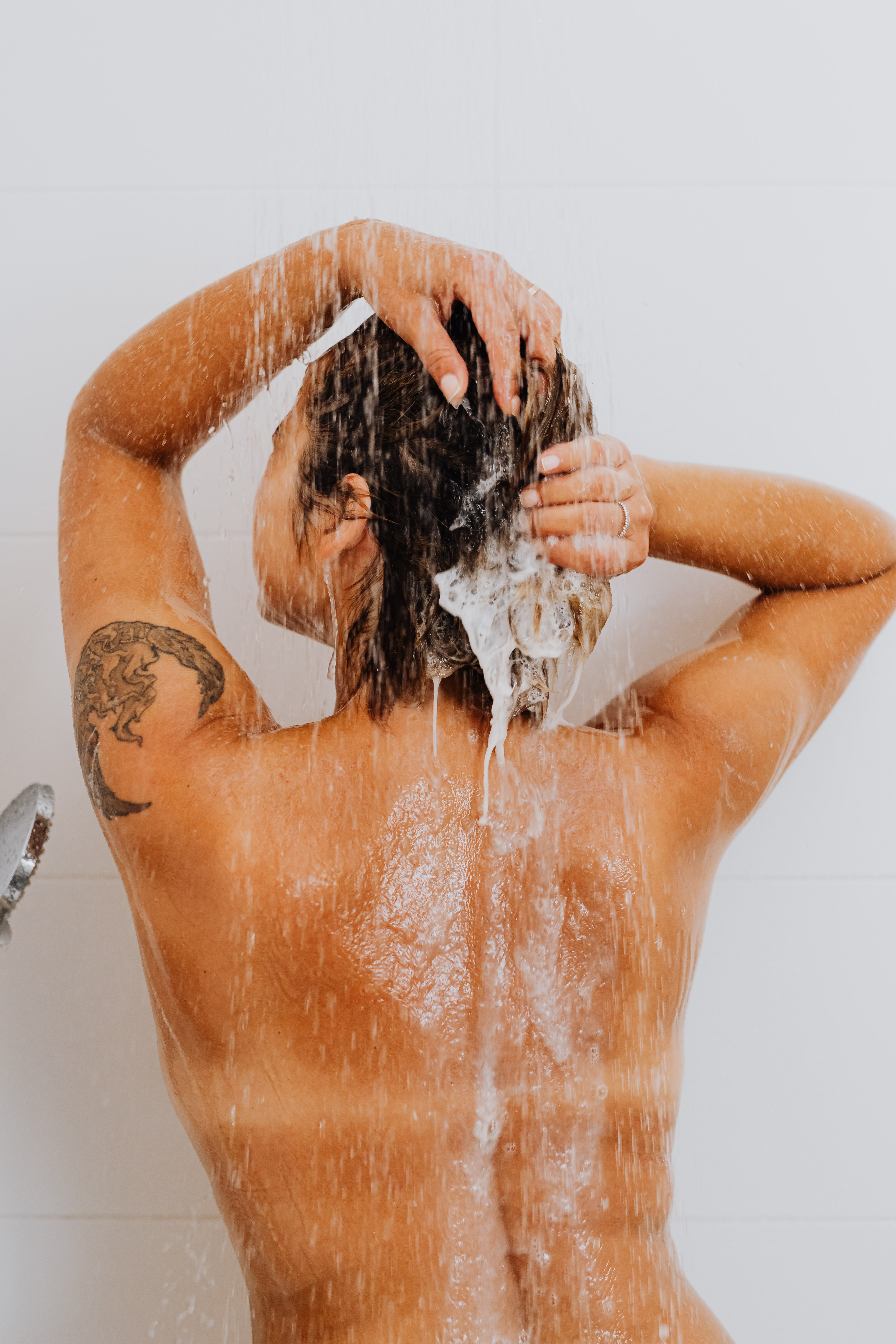 A woman washes her hair while showering. | Source: Pexels