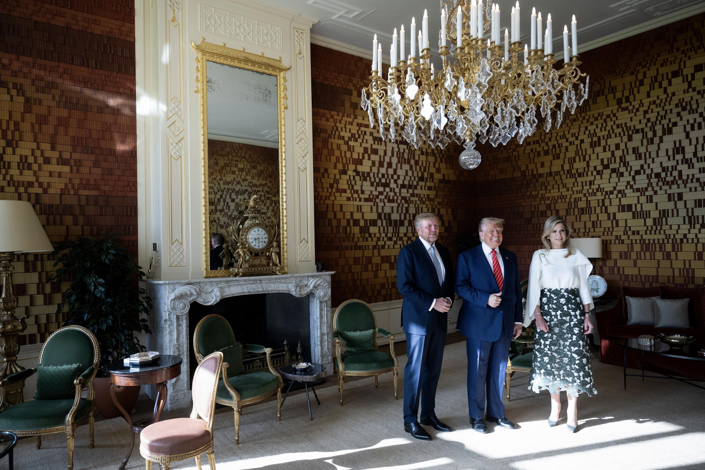 A photo taken from a different angle reveals the elegant room where Trump, King Willem-Alexander, and Queen Máxima posed for their friendly photo. The space features a stunning large chandelier, a mirror framed in gold, and a set of beautiful chairs with rich green cushions, adding to the regal charm.
