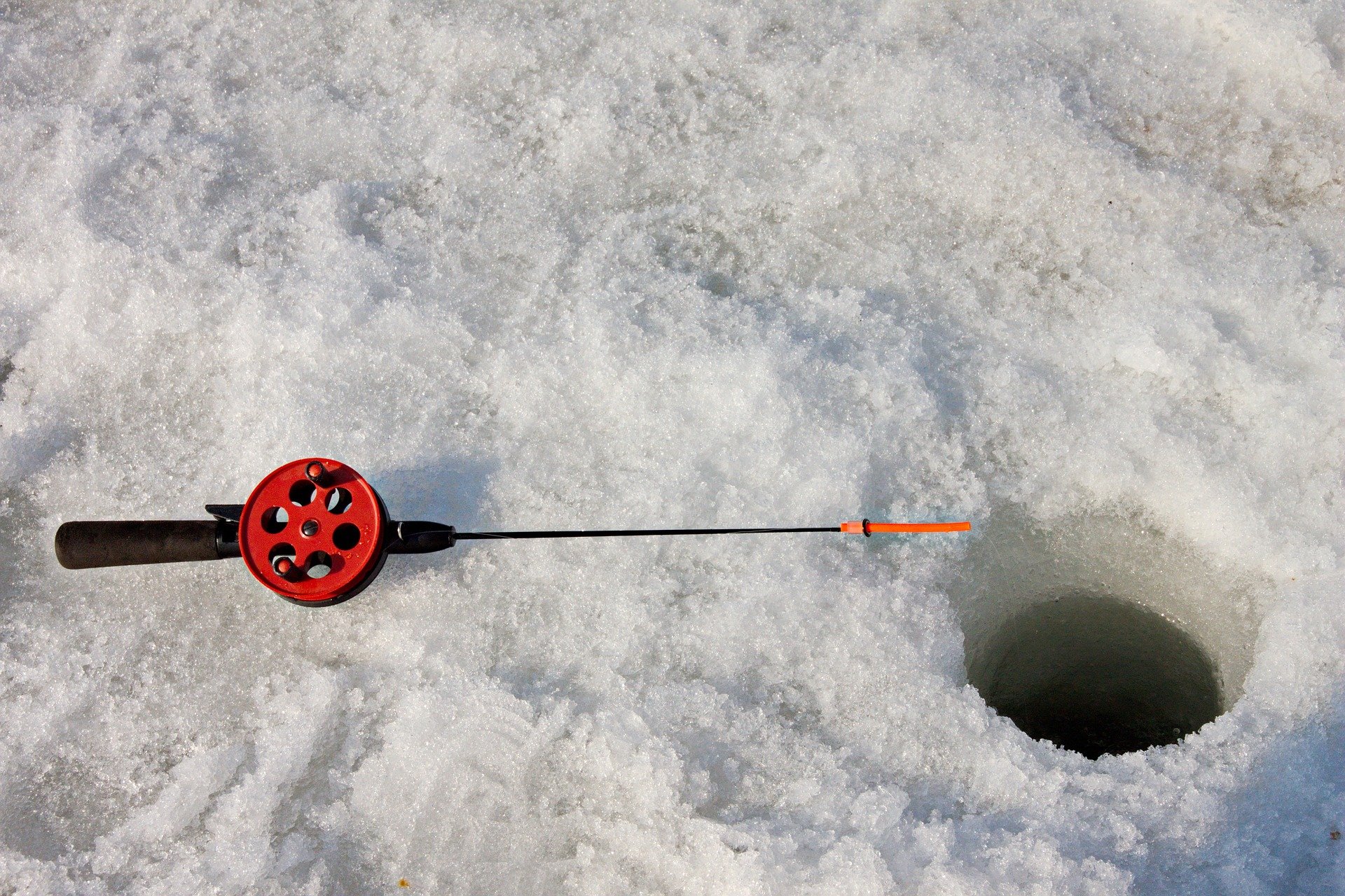A hole in the ice with a fishing rod next to it. | Source: Pixabay.