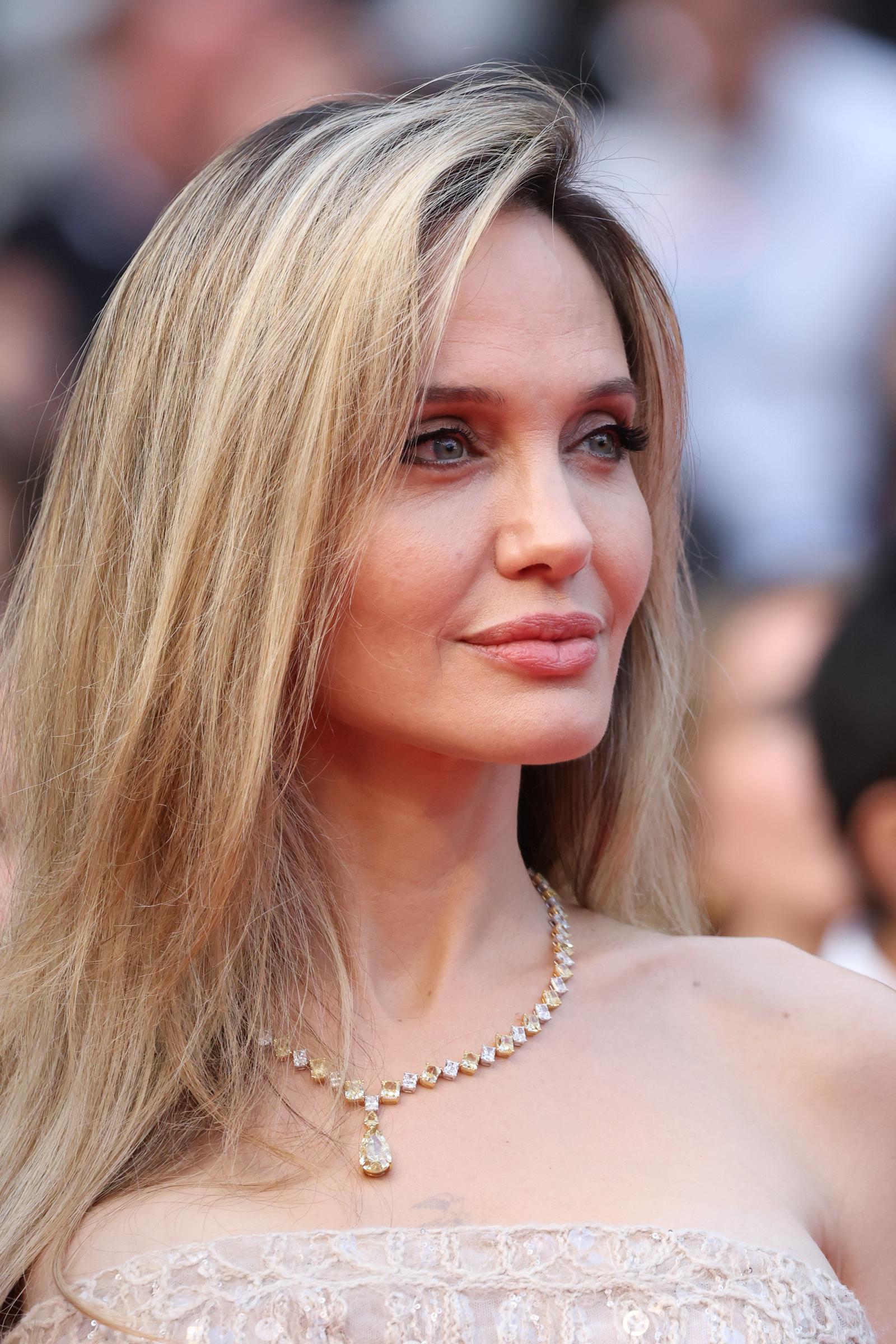In a close-up shot that captures every polished detail, Angelina Jolie’s soft glam makeup and diamond necklace shimmer under the Cannes lights, highlighting her serene expression and golden-hued elegance.