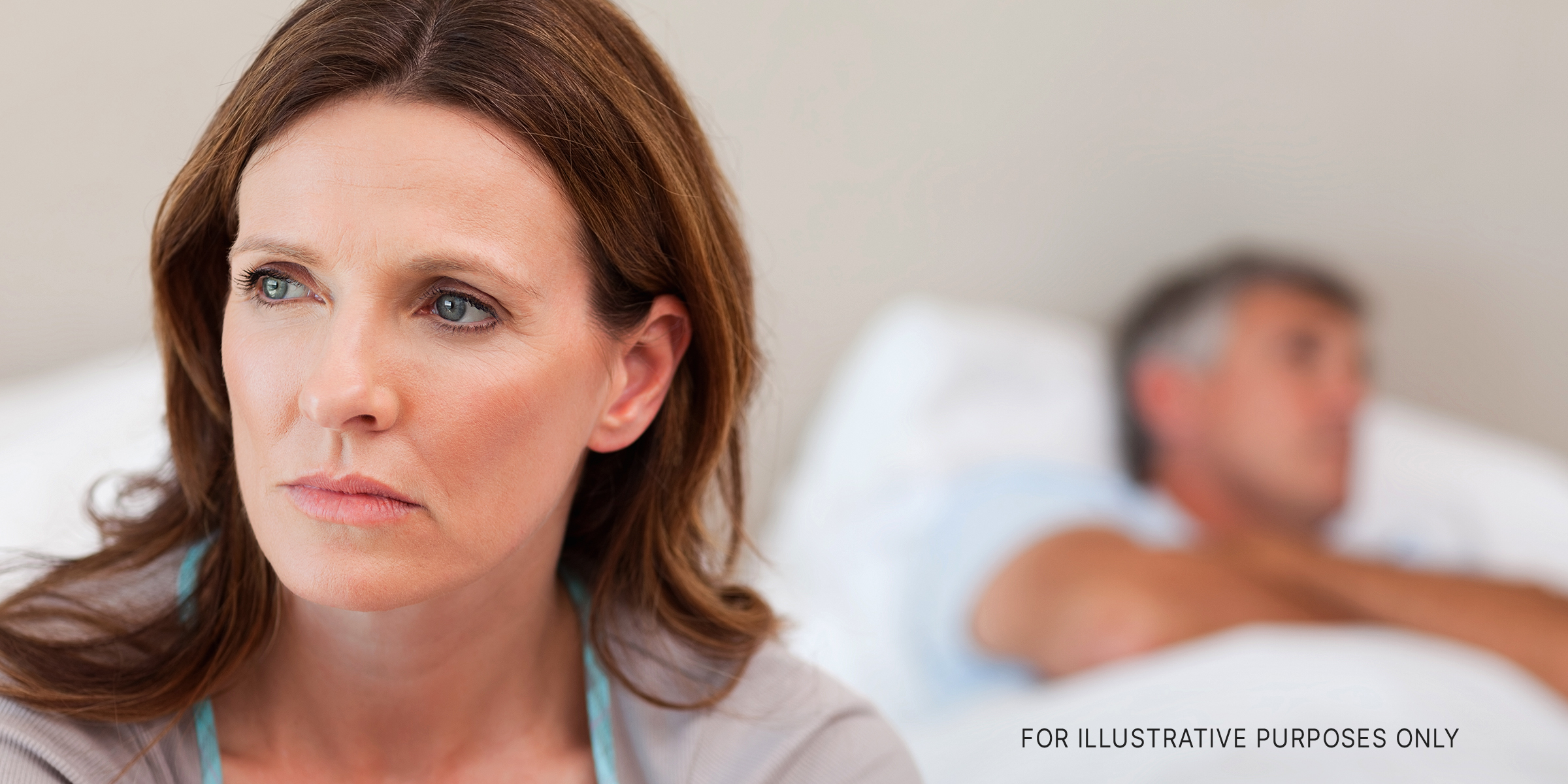 A woman looking sad with a man sleeping in the background | Source: Shutterstock