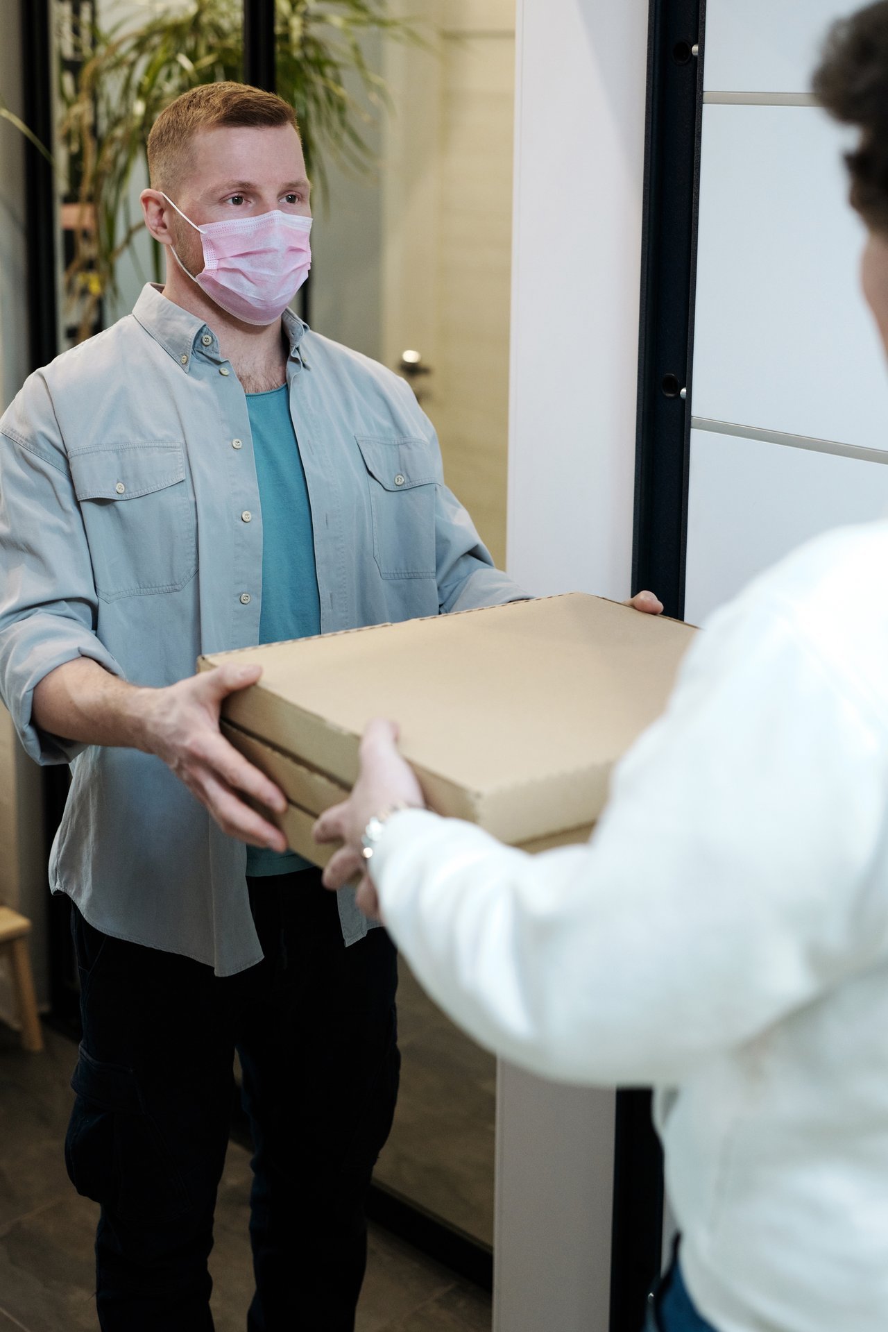 A man wearing a face mask receiving a Pizza delivery | Photo: Pexels