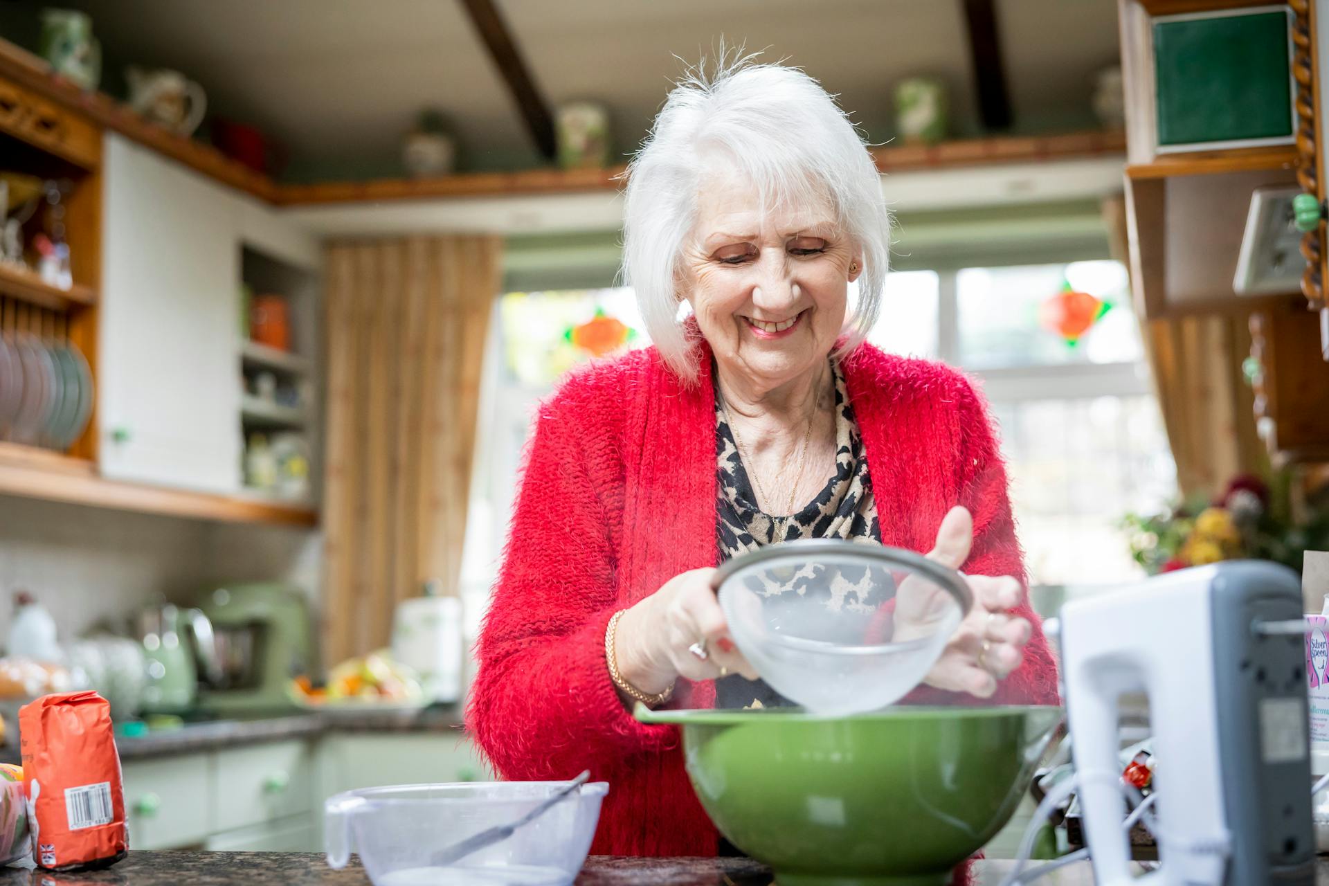 A smiling senior woman sifting flour in her kitchen | Source: Pexels