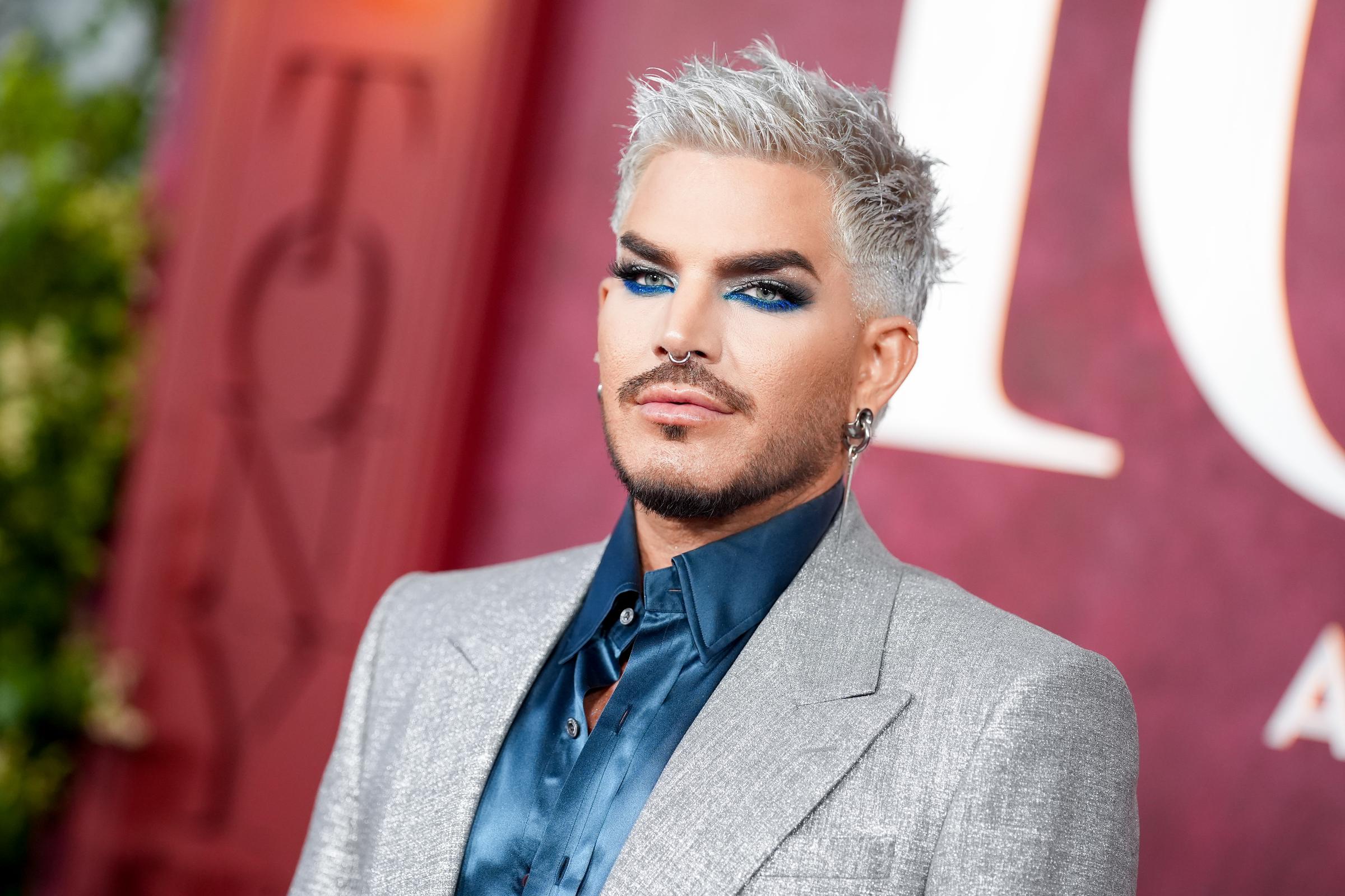 Adam Lambert poses for the cameras in a textured silver blazer and navy satin shirt, accentuated by bold, electric-blue eyeshadow and a dramatic contour. His platinum hair and piercing details added edge to his show-stopping Tony Awards entrance.