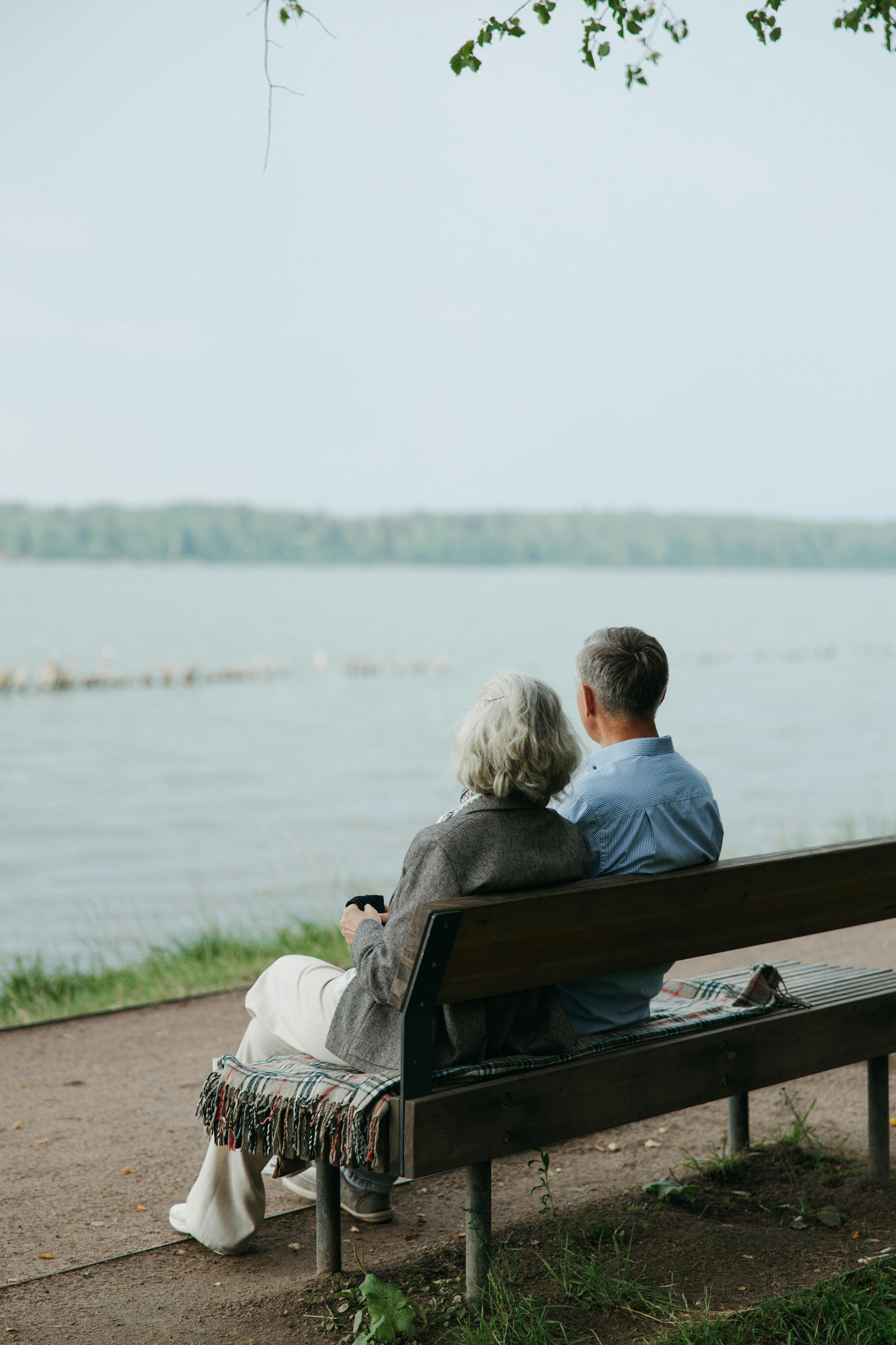 An elderly couple sitting on a bench by the lake | Source: Pexels