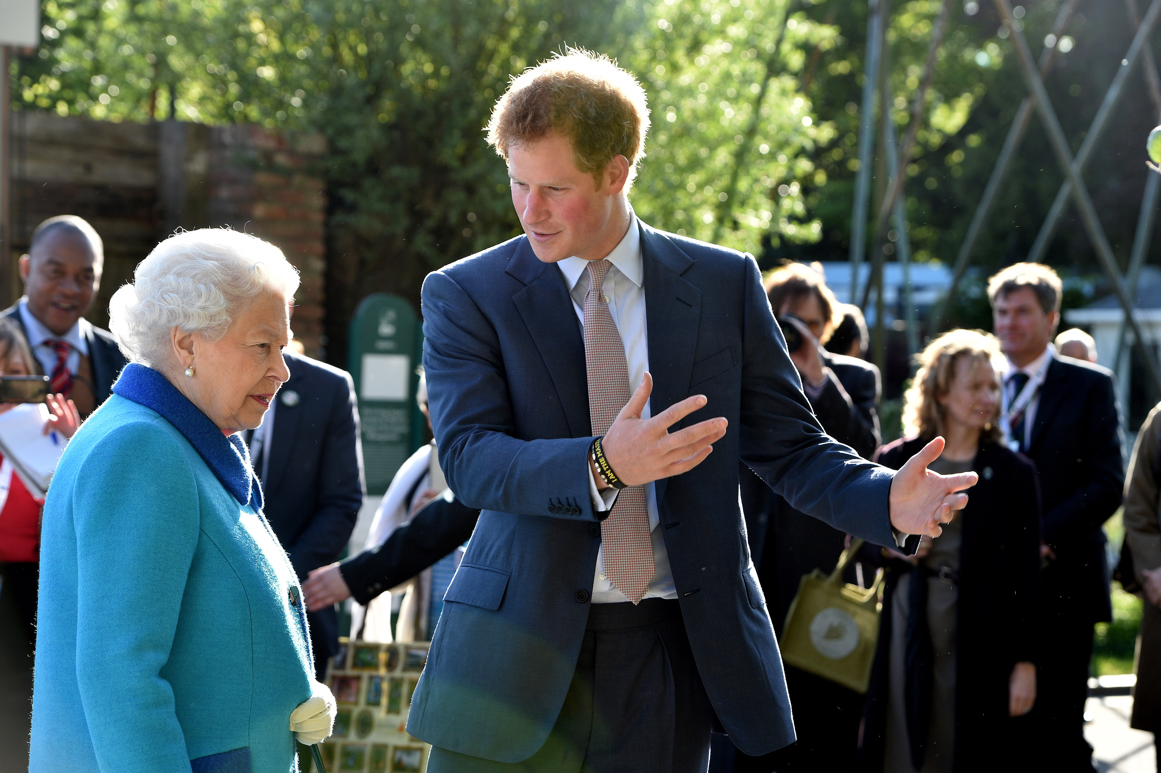 Queen Elizabeth II and Prince Harry were seen sharing a focused moment as they toured the Chelsea Flower Show at the Royal Hospital Chelsea on 18 May 2015, with the Duke of Sussex gesturing animatedly as if explaining a display. Dressed in a tailored navy suit, Prince Harry appeared relaxed and engaged, while the late monarch, in a bright blue coat, listened attentively.