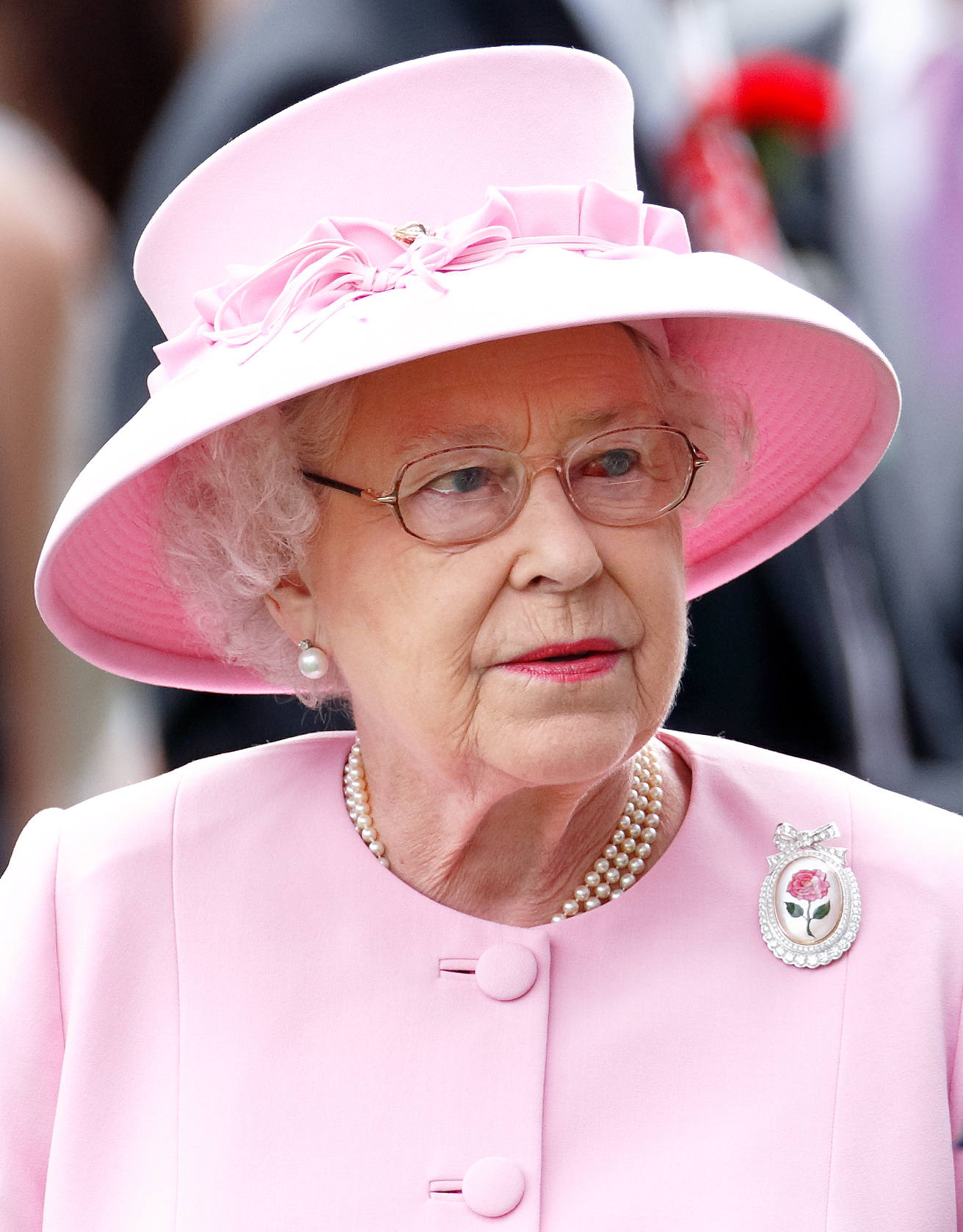 On the Royal Ascot's second day, Queen Elizabeth II dons her commissioned Centenary Rose Brooch and pink attire. The red discoloration in her left eye is visible as she interacts with attendees.