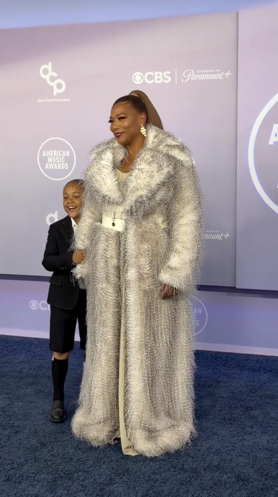 Queen Latifah keeps her focus on the cameras while Rebel Nichols Owens peeks out beside her oversized silver coat at the 2026 American Music Awards. | Source: Instagram/perezhilton