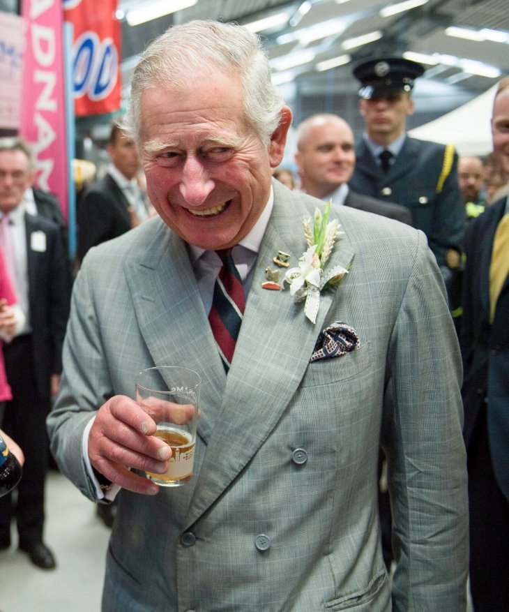 Le prince Charles souriant et tenant un verre dans un costume gris carreaux | Photo : Getty Images