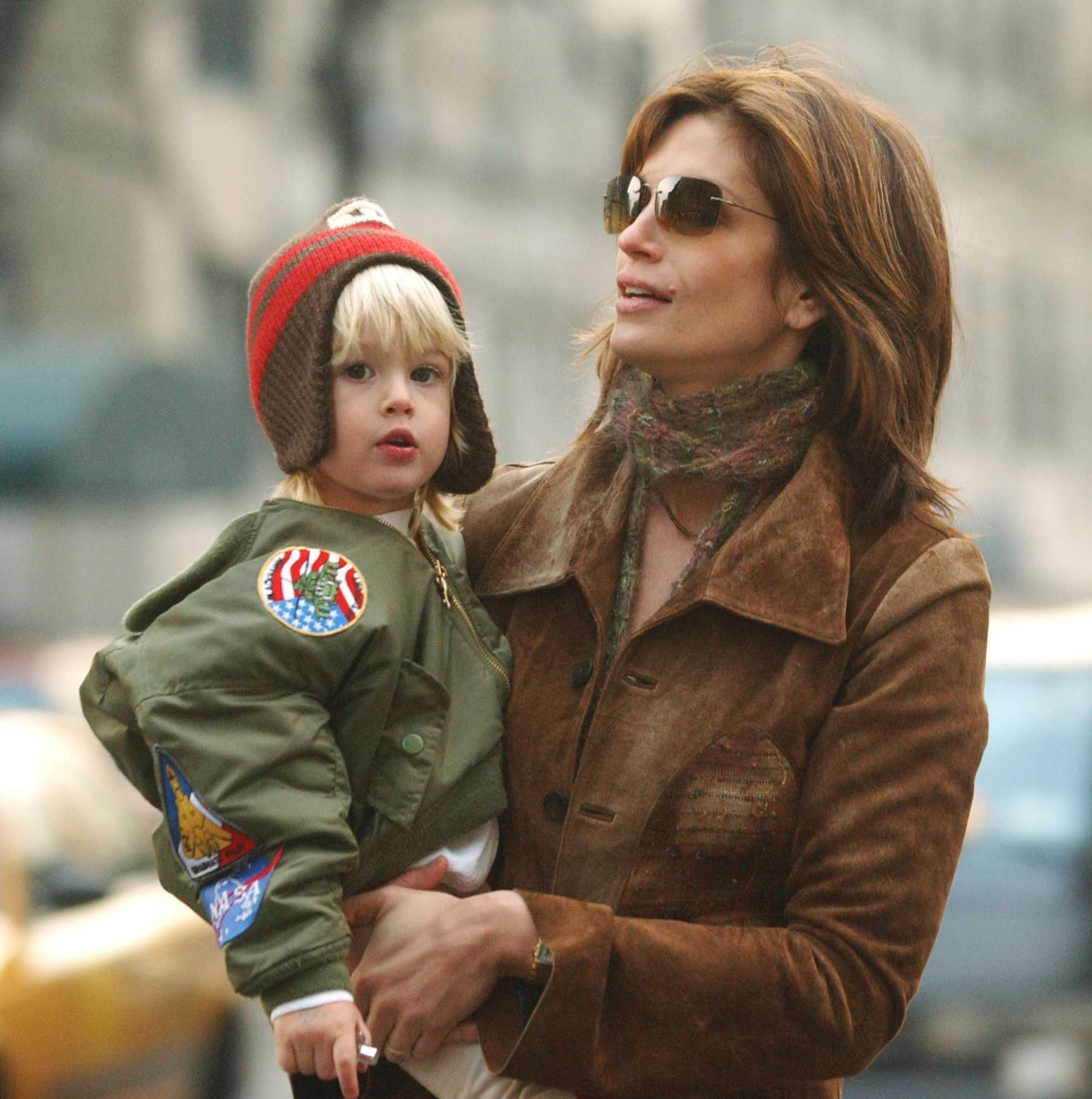 Cindy Crawford holds a wide-eyed Presley Gerber during a walk through New York City on March 8, 2002. Dressed in an aviator-style jacket adorned with space-themed patches and a knit hat with ear flaps, Presley stands out with his golden hair and cherubic face — an early glimpse of the camera-ready features that would later land him in fashion campaigns.