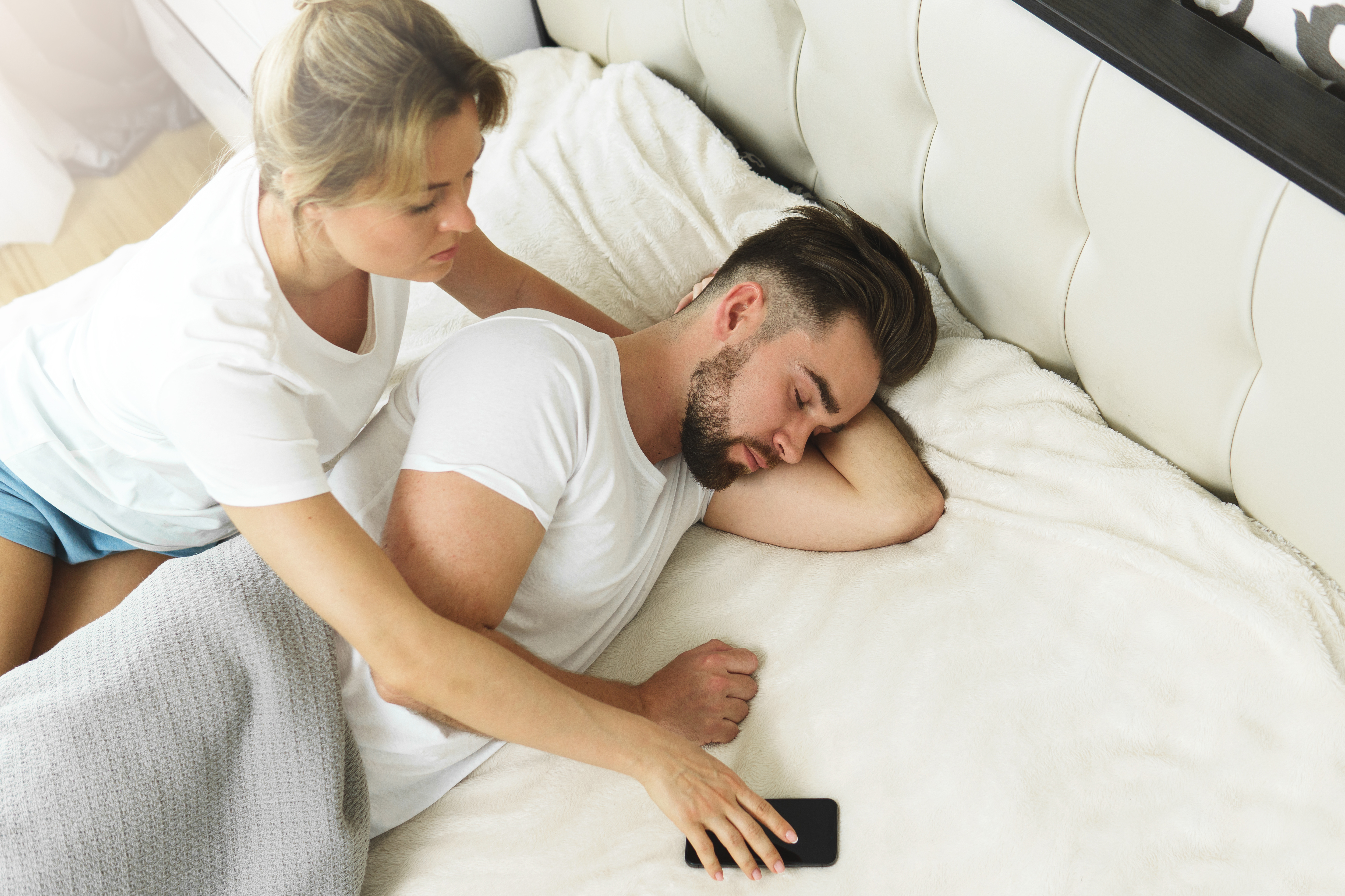A woman trying to take her partner's phone while he sleeps | Source: Shutterstock