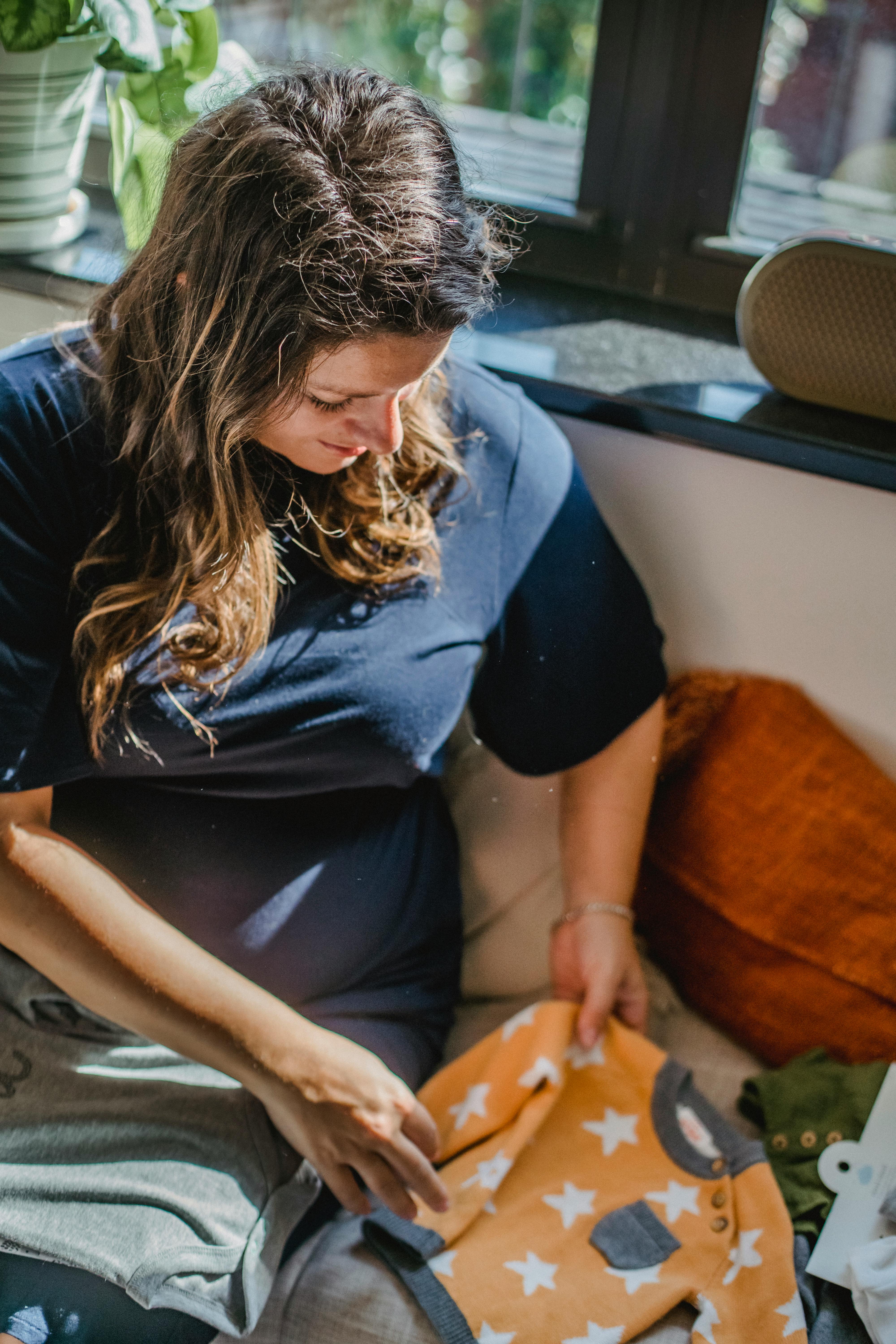 A pregnant woman sitting with baby clothes | Source: Pexels