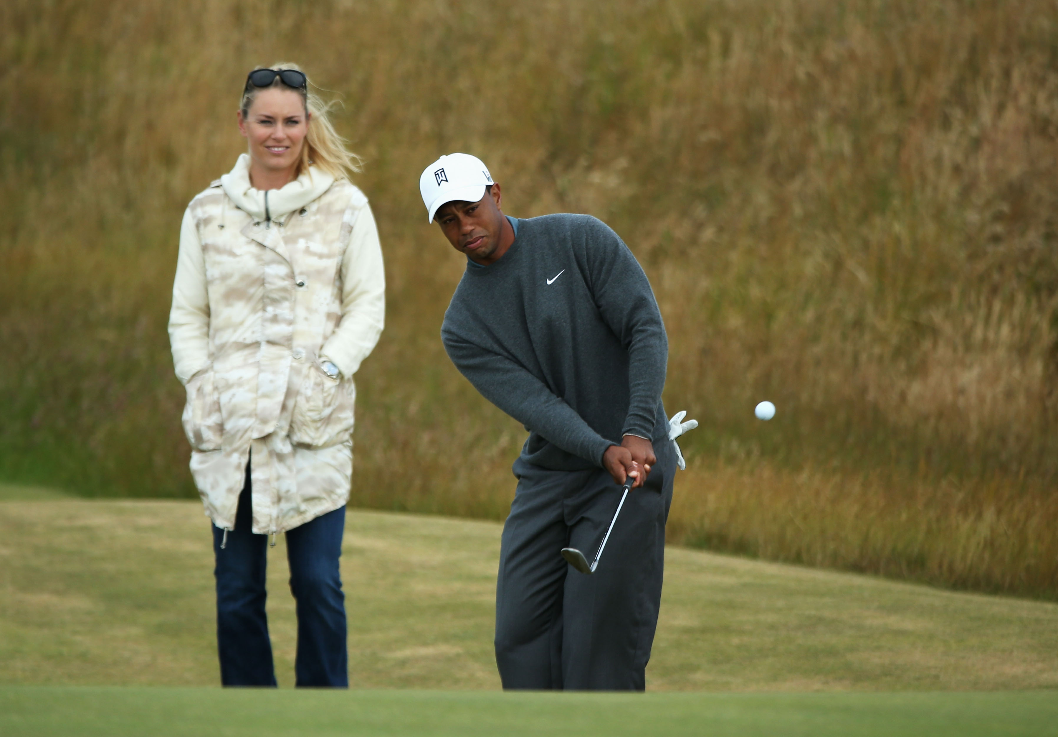 Tiger Woods chips the ball while Lindsey Vonn watches at the 142nd Open Championship on July 15, 2013, in Gullane, Scotland | Source: Getty Images