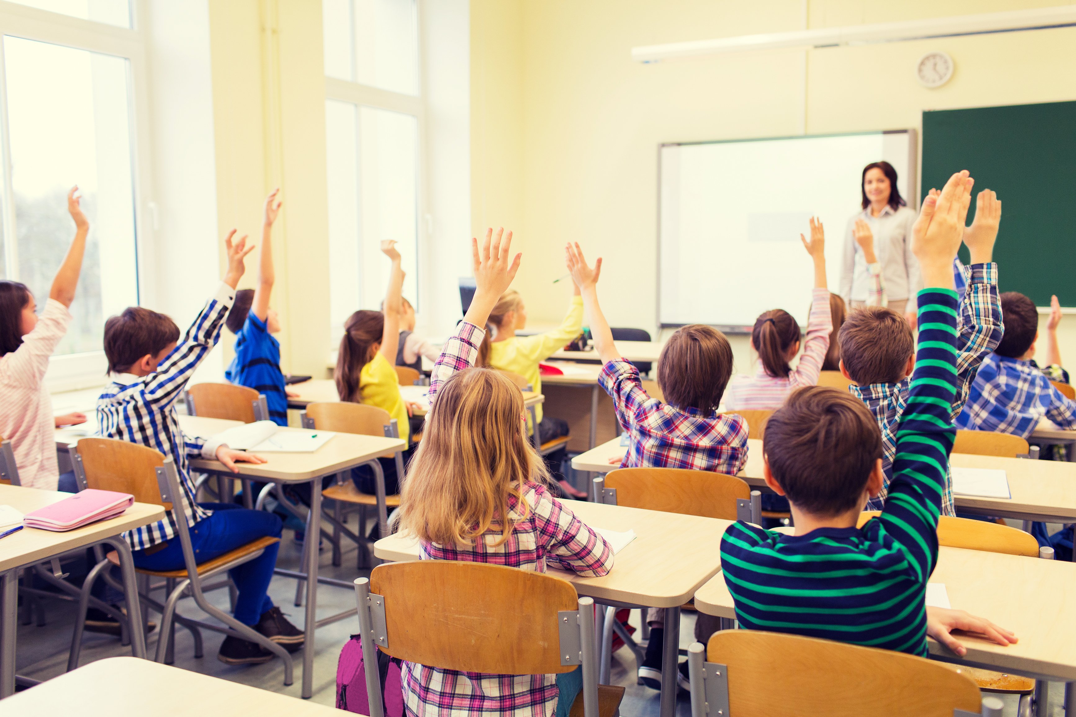 Group of school kids with teacher sitting in classroom and raising hands | Photo: Shutterstock