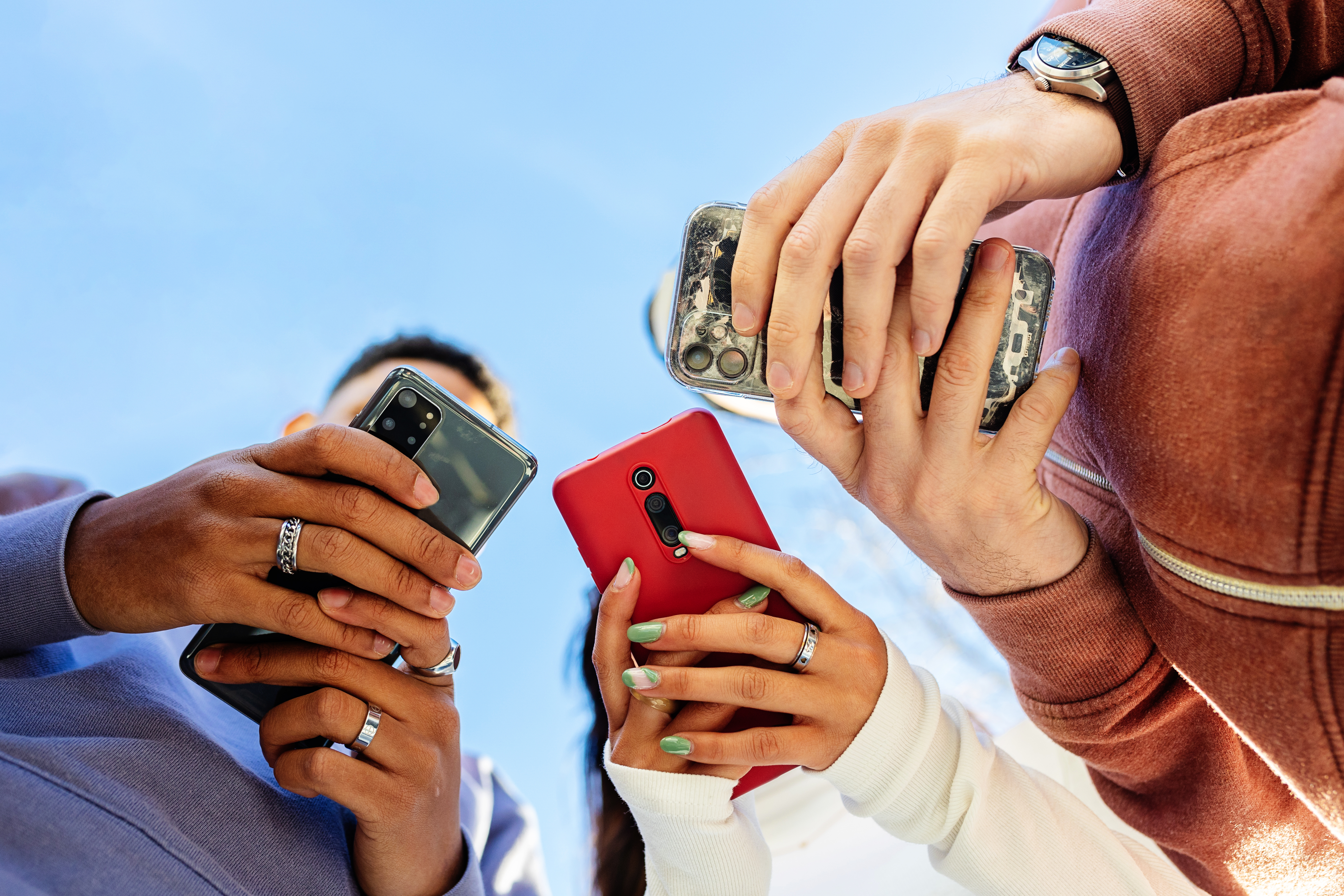 Low angle view of three young people using mobile phones outdoors | Source: Getty Images