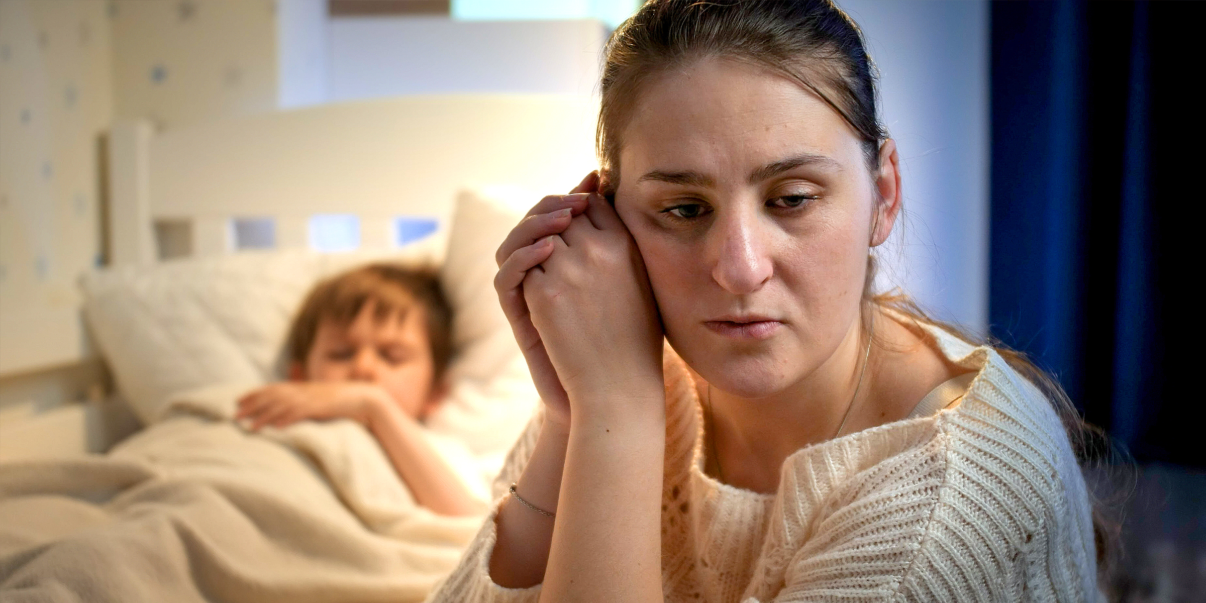 An upset woman sitting beside a child sleeping in his bed | Source: Shutterstock
