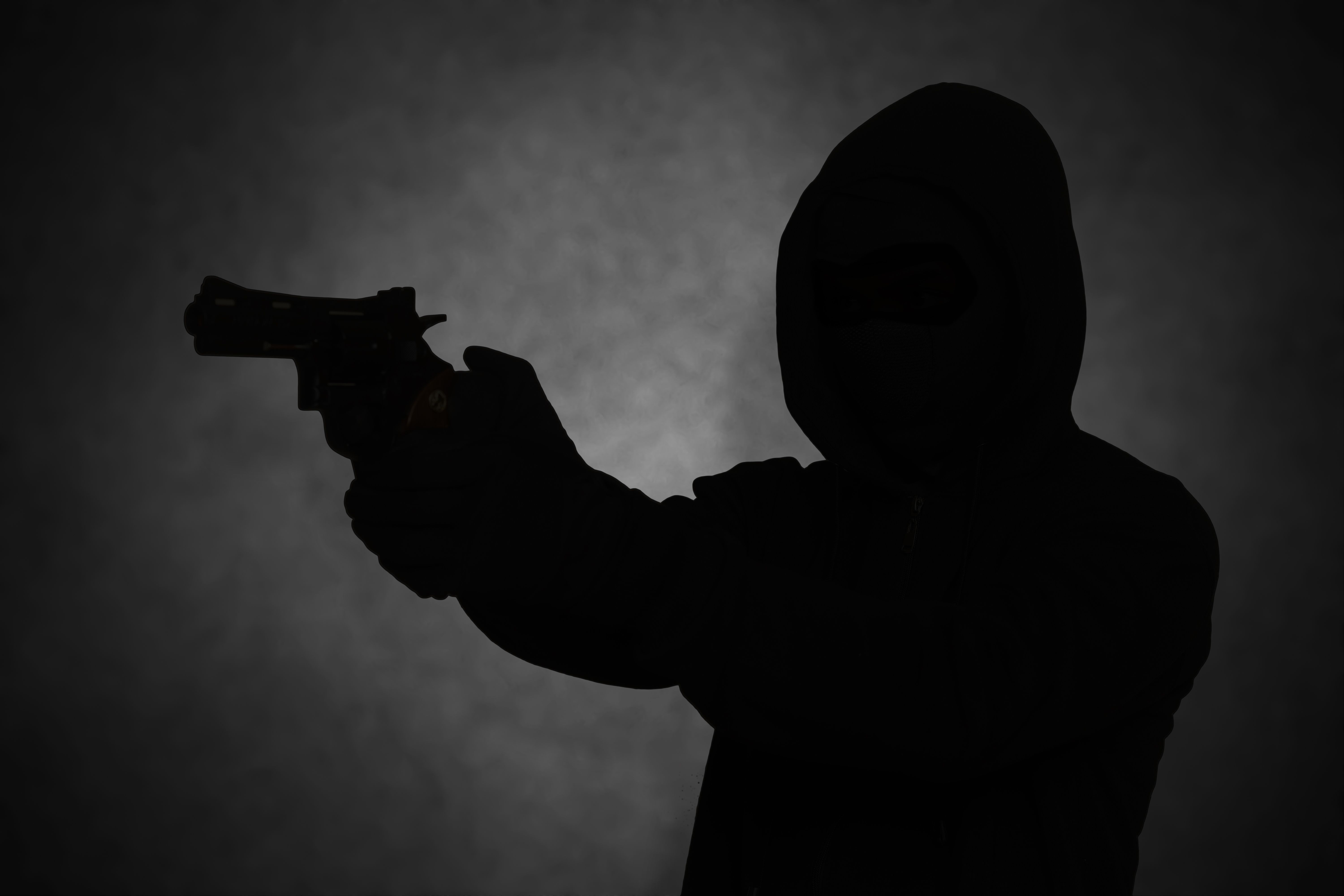Mysterious man wearing black hoodie holding a pistol, shooting with a gun. | Source: Shutterstock