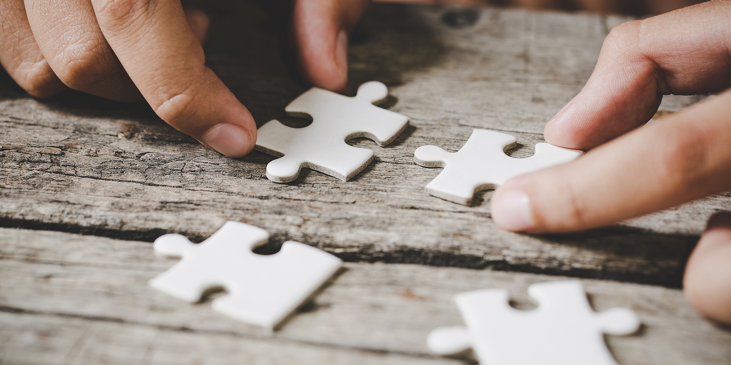 A person holding the pieces of a white jigsaw puzzle on a wooden surface | Source: Freepik