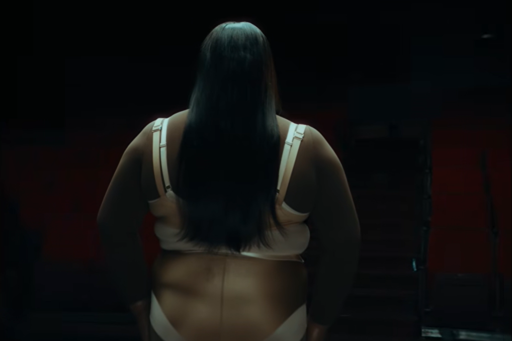 A rear view introduces the earlier version in a dim theater setting | Source: YouTube/Lizzo