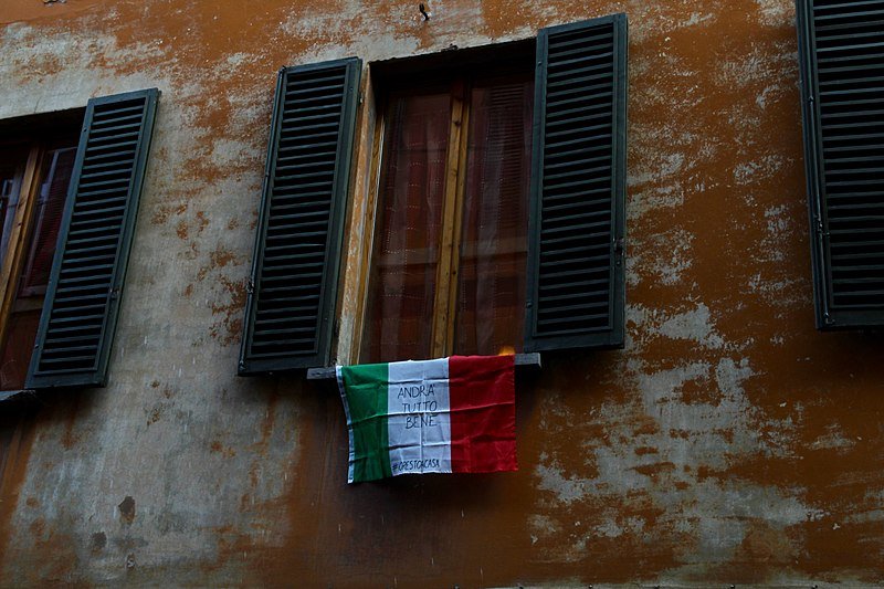 Un drapeau italien accroché à une fenêtre de Bologne avec le slogan "Tout va bien se passer"| Photo : Wikipedia/Pietro Luca Cassarino