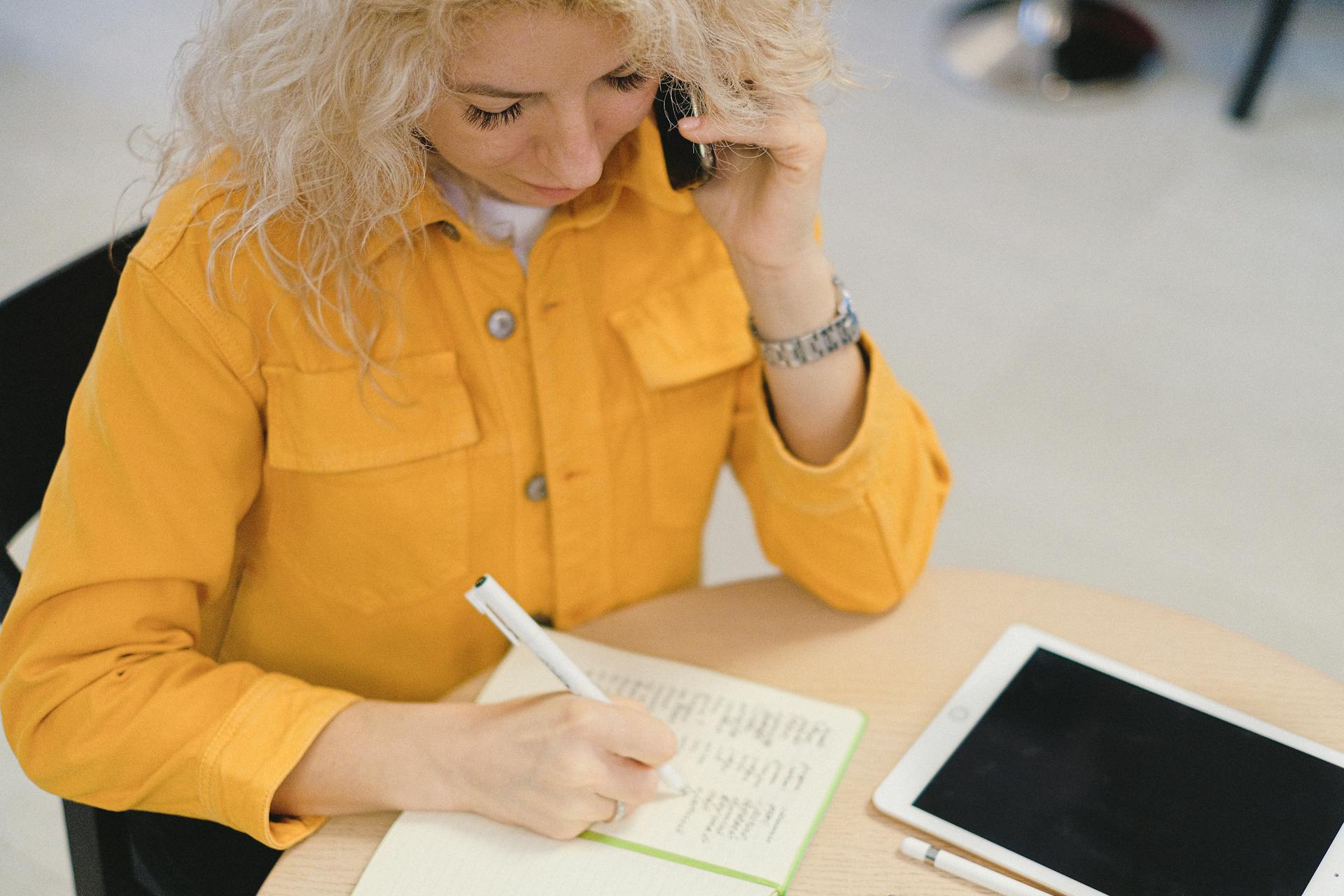 A woman writing in her notebook while attending a call | Source: Pexels