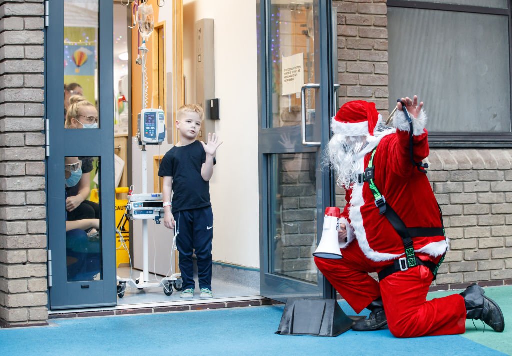 A man dressed as Santa Claus kneels outside the building as he speaks to Ellis Harkin through an open doorway as he visits patients at Leeds Children's Hospital on Mon. December 21, 2020  | Photo: Getty Images