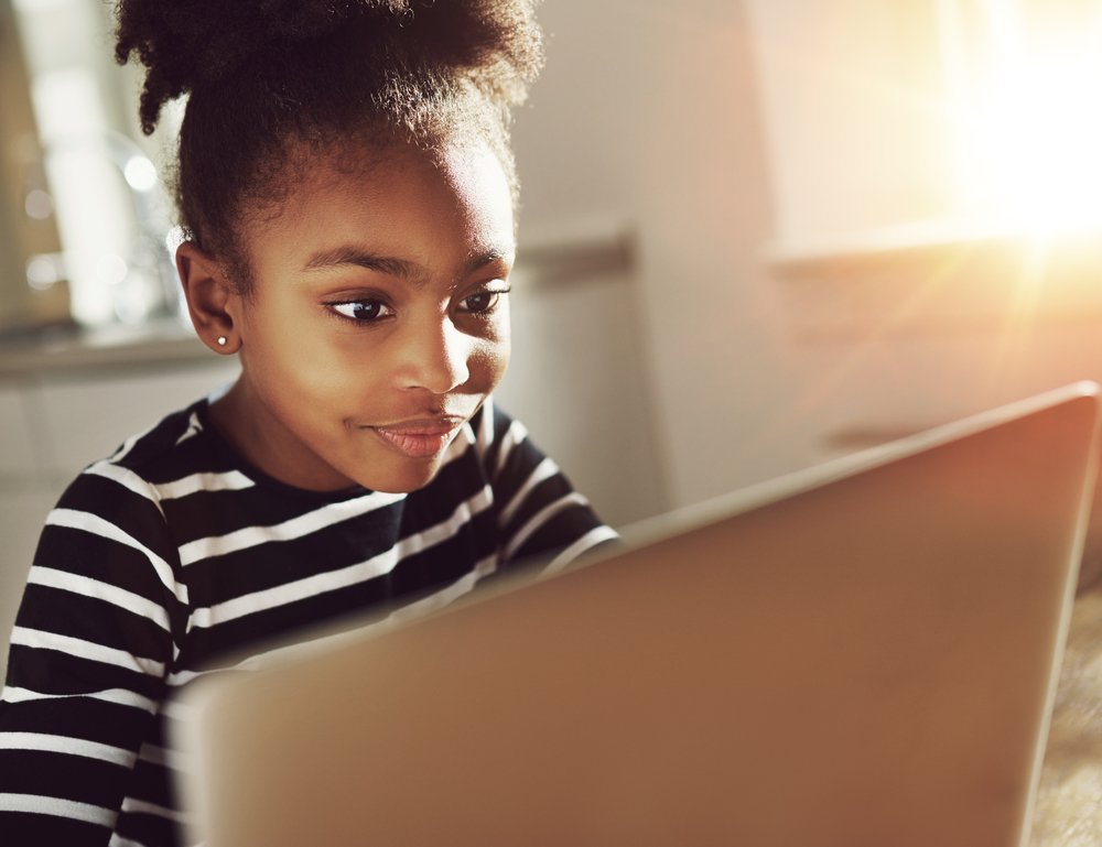 Smiling young girl is absorbed in laptop use | Photo: Getty Images Smiling young girl is absorbed in laptop use | Photo: Getty Images