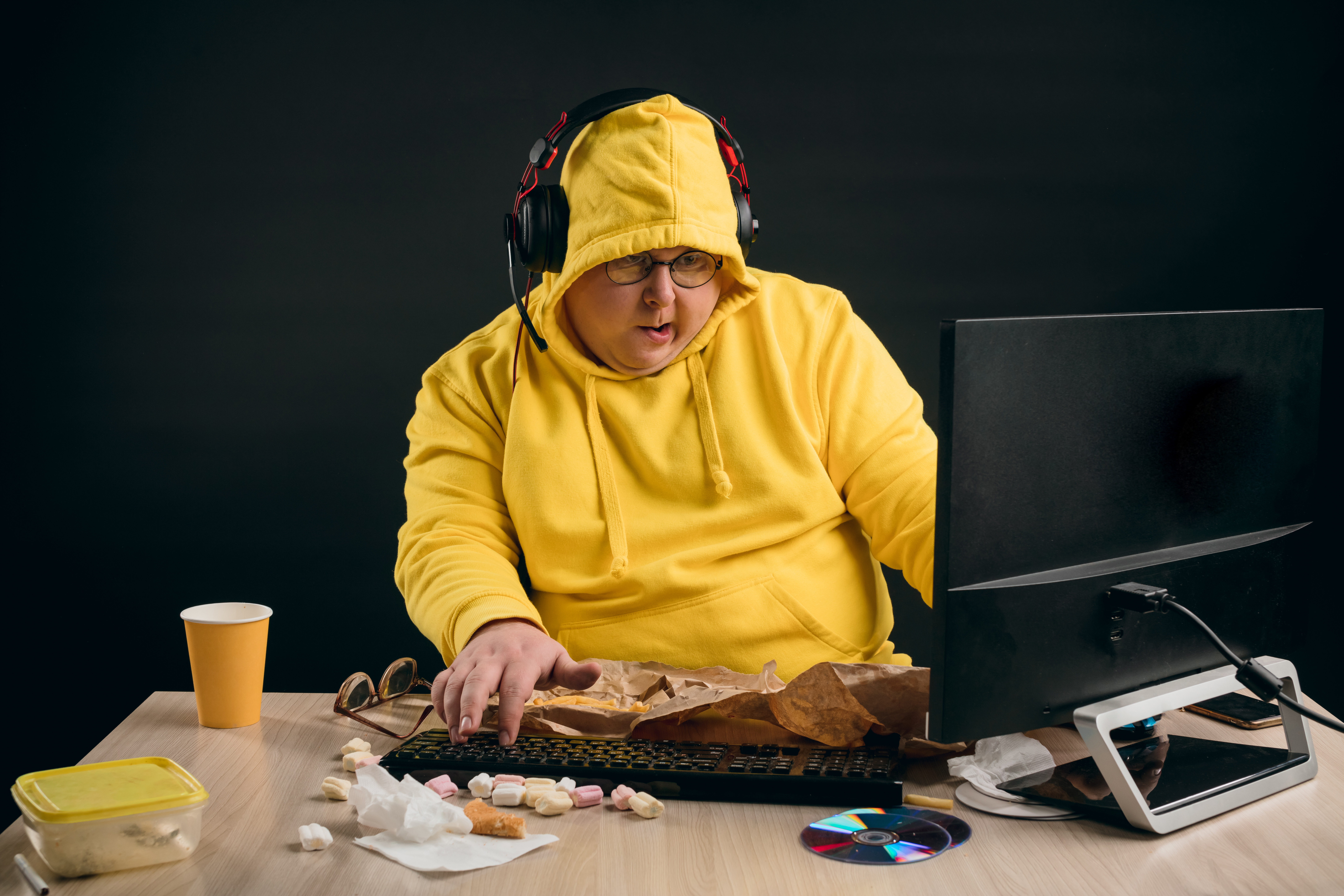 A man in a hoodie sitting behind a messy desk | Source: Shutterstock