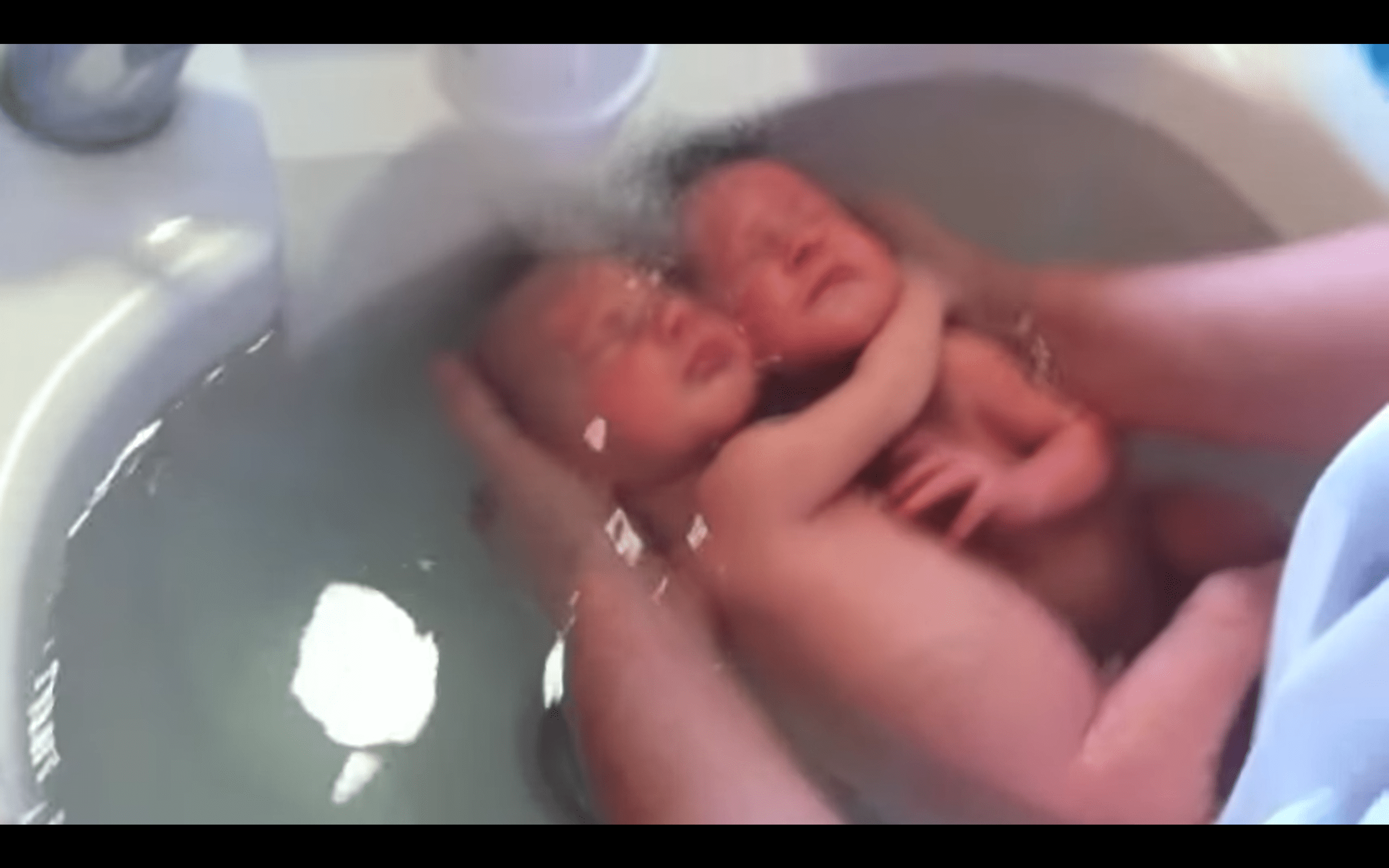 Twin babies holding on to each other in a video shared by a nurse bathing them. | Photo: youtube.com/massagebebe